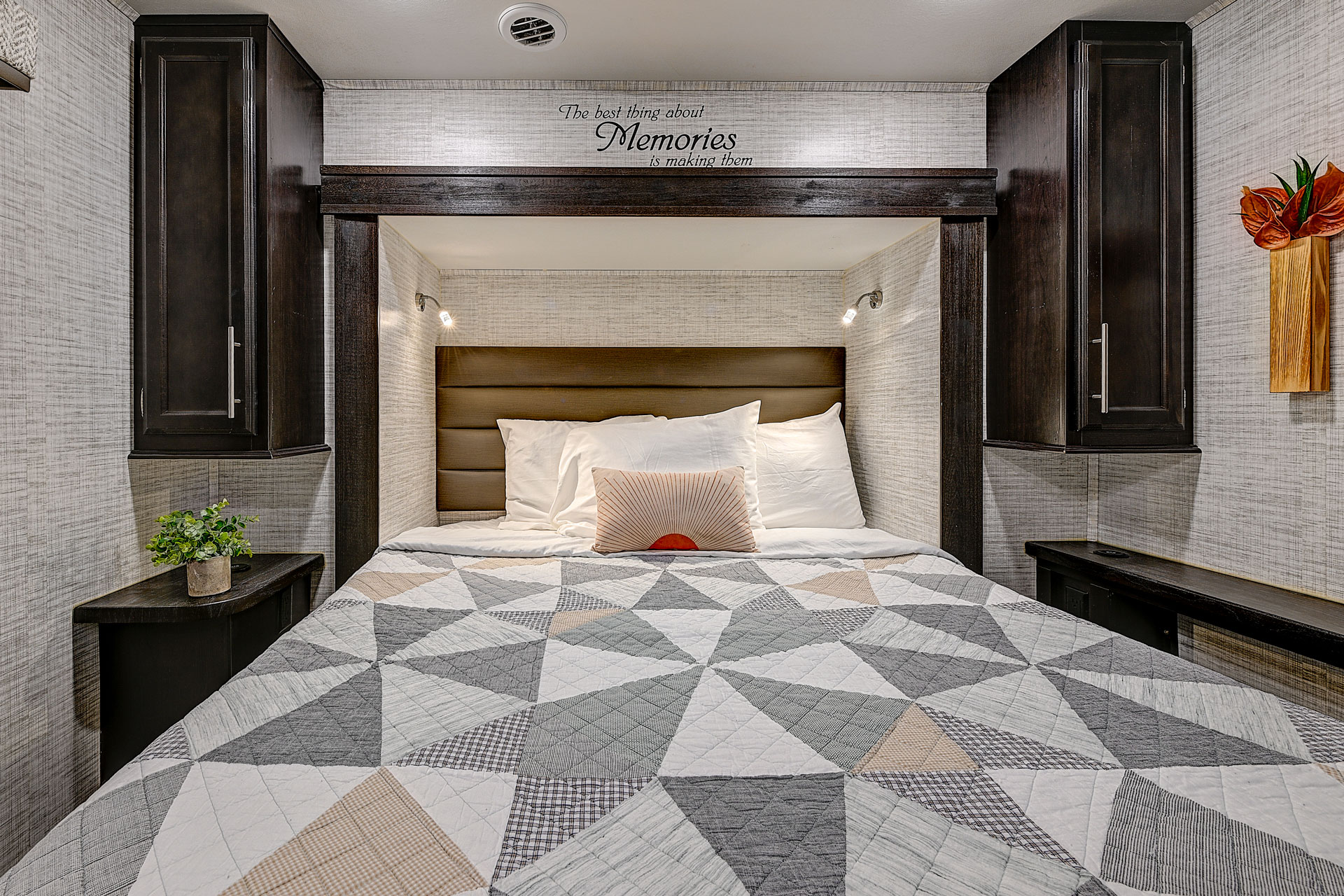 Cozy RV rental bedroom with a geometric quilted bed, dark wood built-ins, reading lights, and an inspiring quote above the bed.. Entegra Coach Odyssey 2024