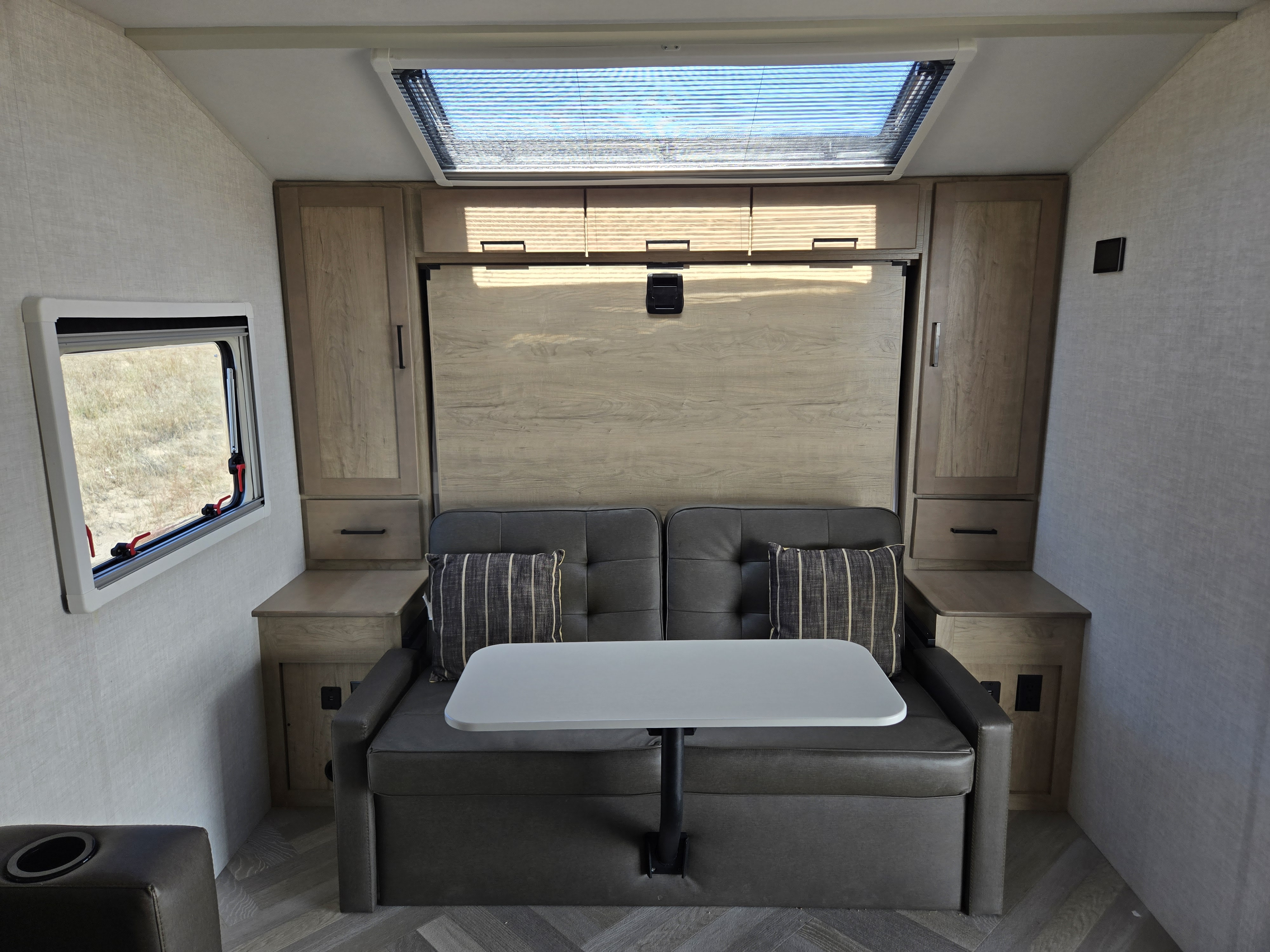 RV rental interior features a sofa, attached dining table, overhead murphy bed, storage cabinets, and skylight.. Ember Overland 2021