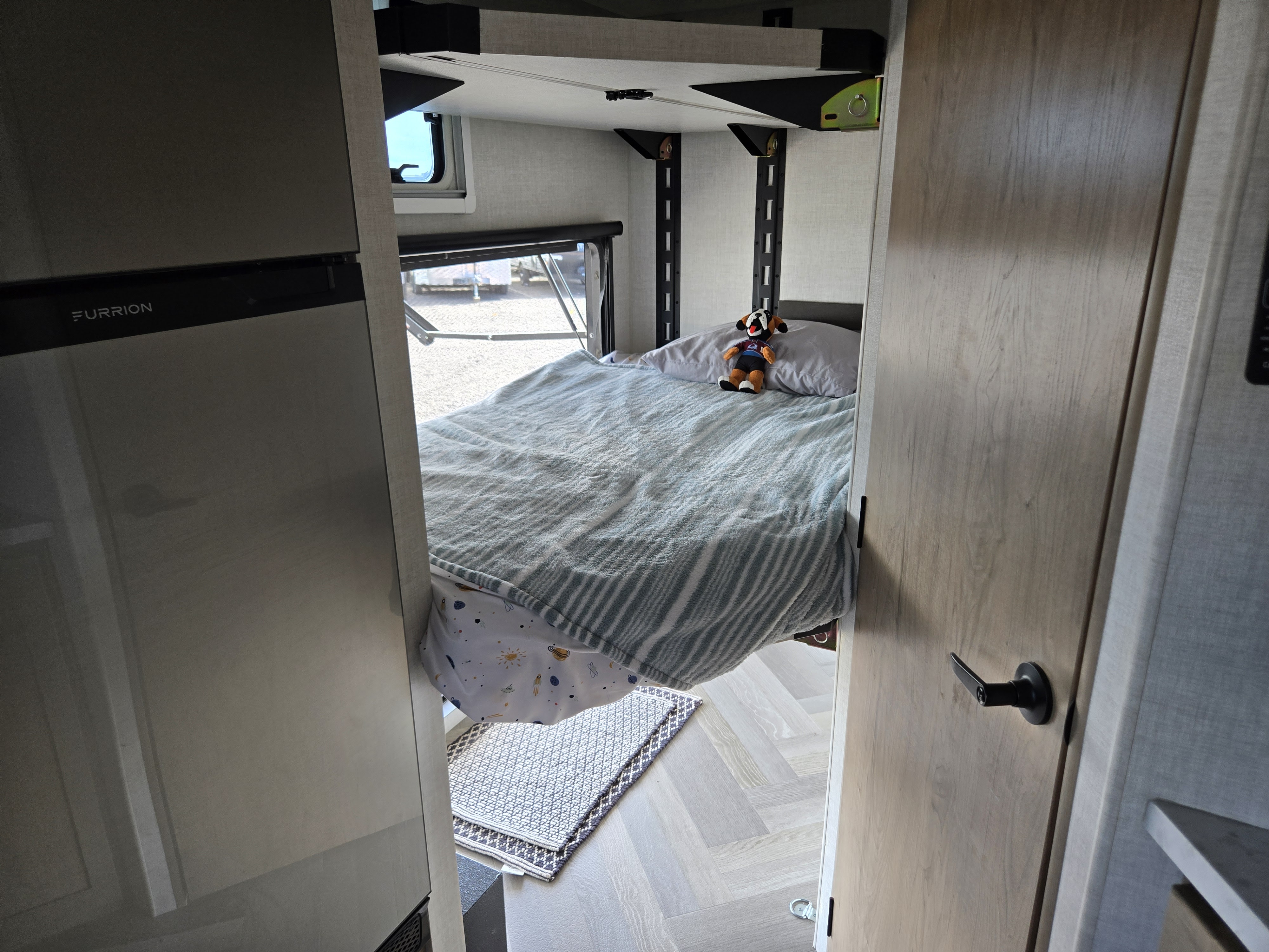 Cozy RV rental interior featuring a bunk bed with a plush toy, Furrion fridge on the left, and a modern door.. Ember Overland 2021