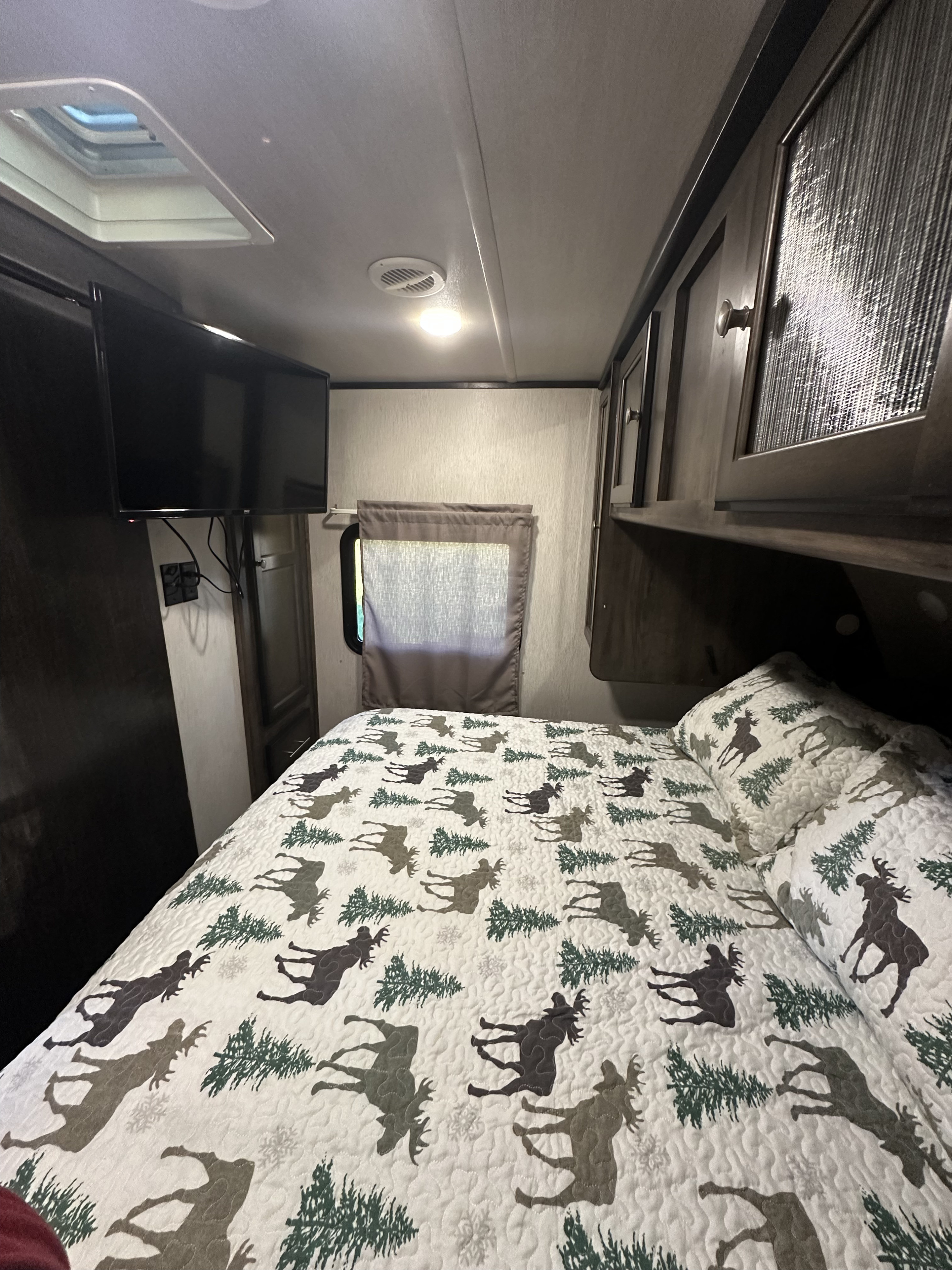 Cozy RV rental bedroom with a mounted TV, overhead storage, and a unique moose-patterned quilt for comfortable travel.. Heartland RVs Mallard 2020