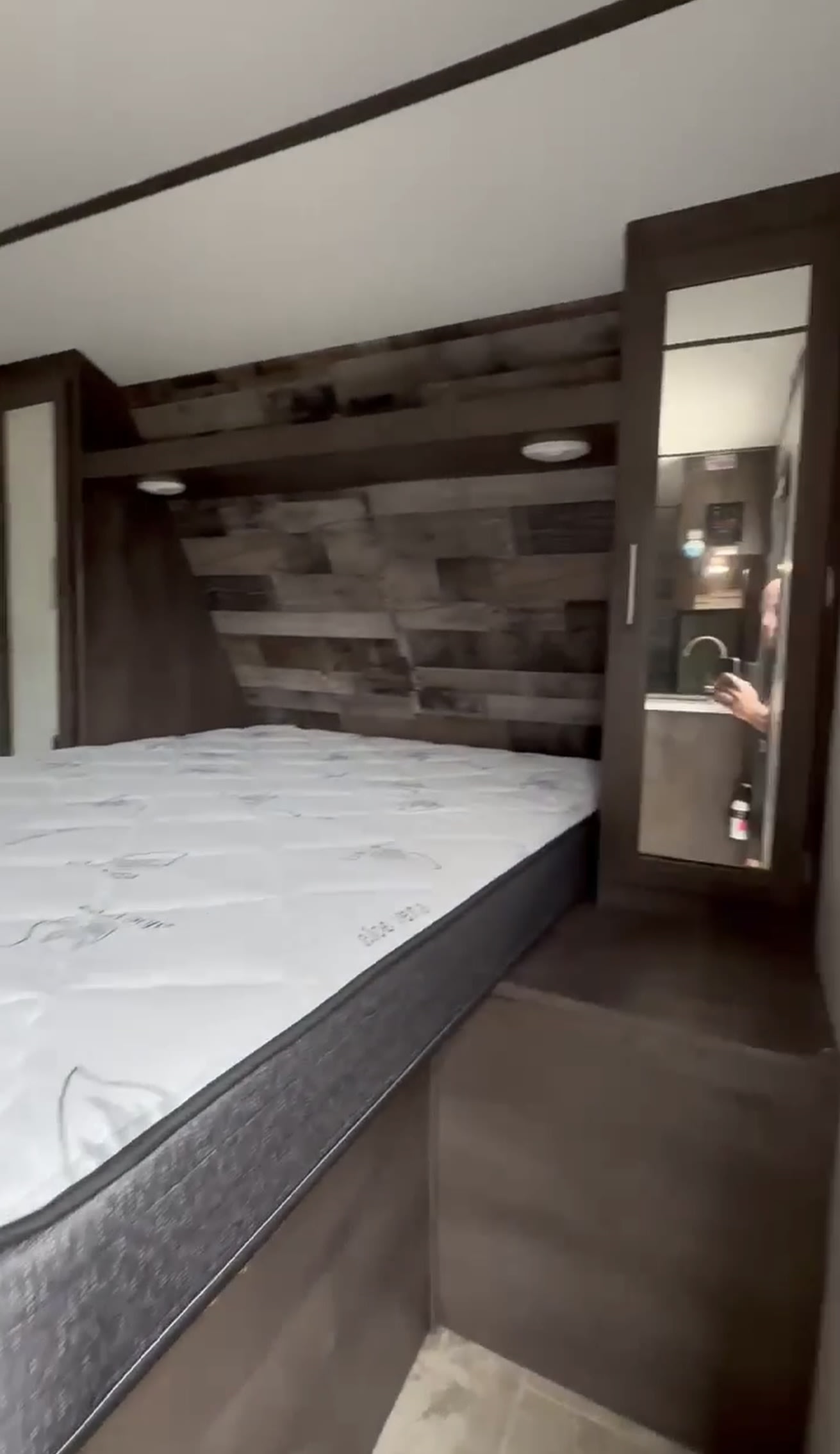 Spacious RV rental bedroom with a comfy mattress and built-in storage. Mirror reflects a peek into the kitchen area.. Aspen Trail 2180RDWE 2020