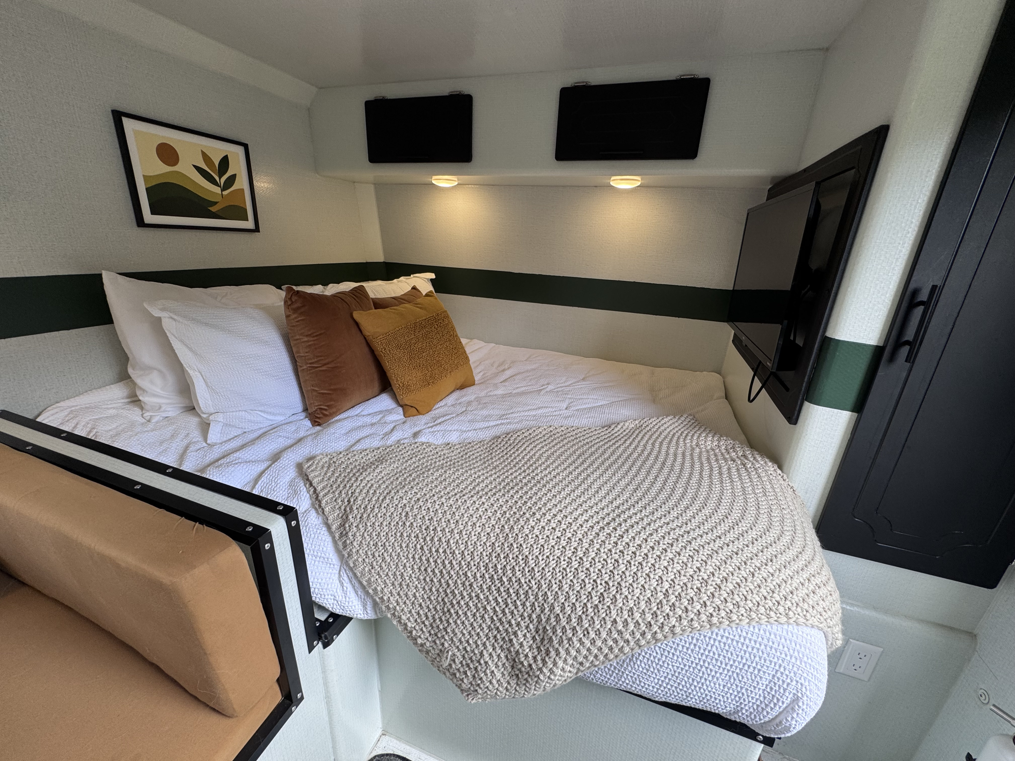 Cozy RV rental bedroom featuring a bed with earthy pillows, a wall-mounted TV, minimalist art, and smart storage.. LIV LIV Trailer 2024