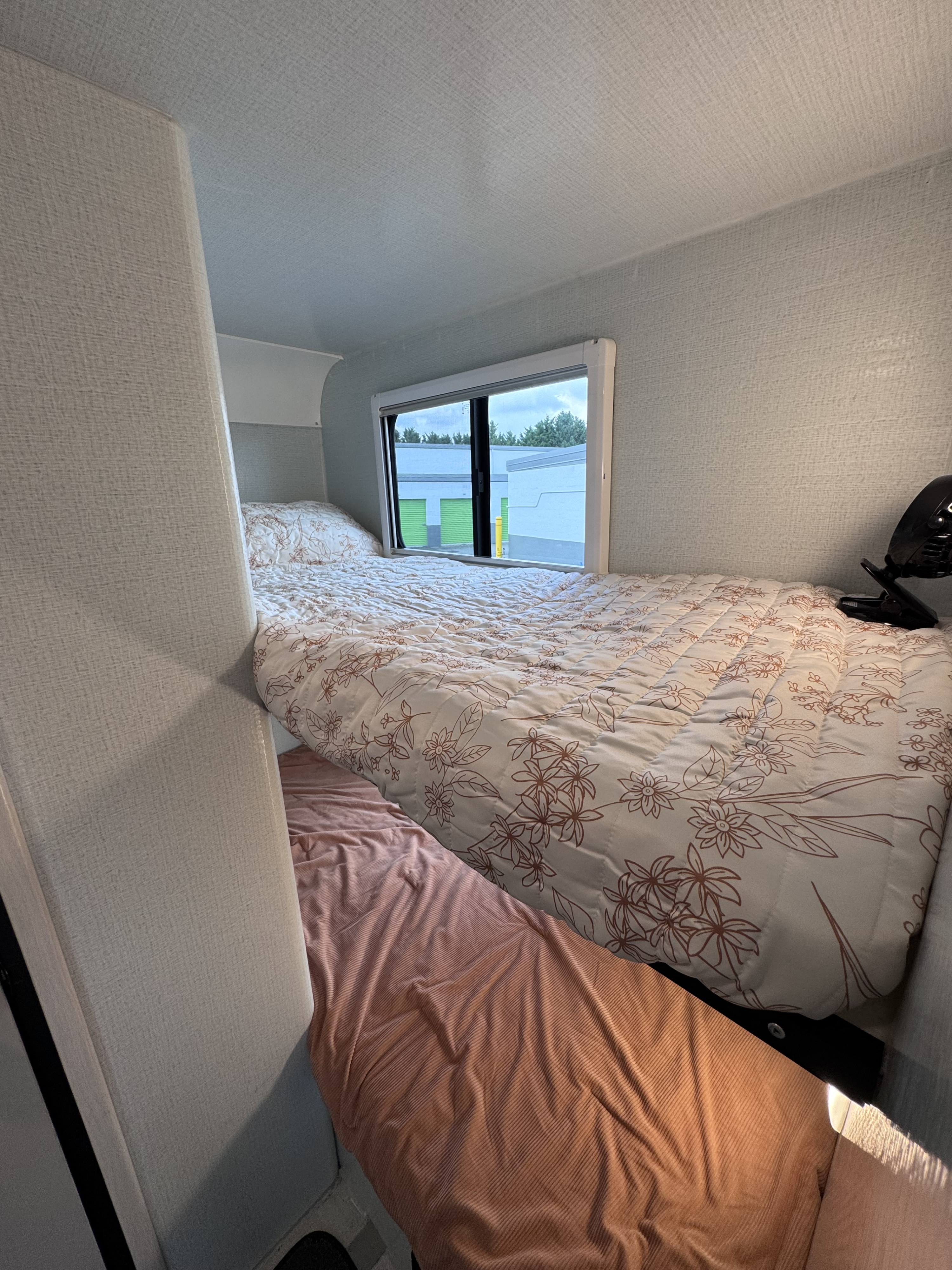 Cozy rv rental bunk beds. Upper bed has a floral comforter; lower bed has a pink sheet. Window view of buildings.. LIV LIV Trailer 2024