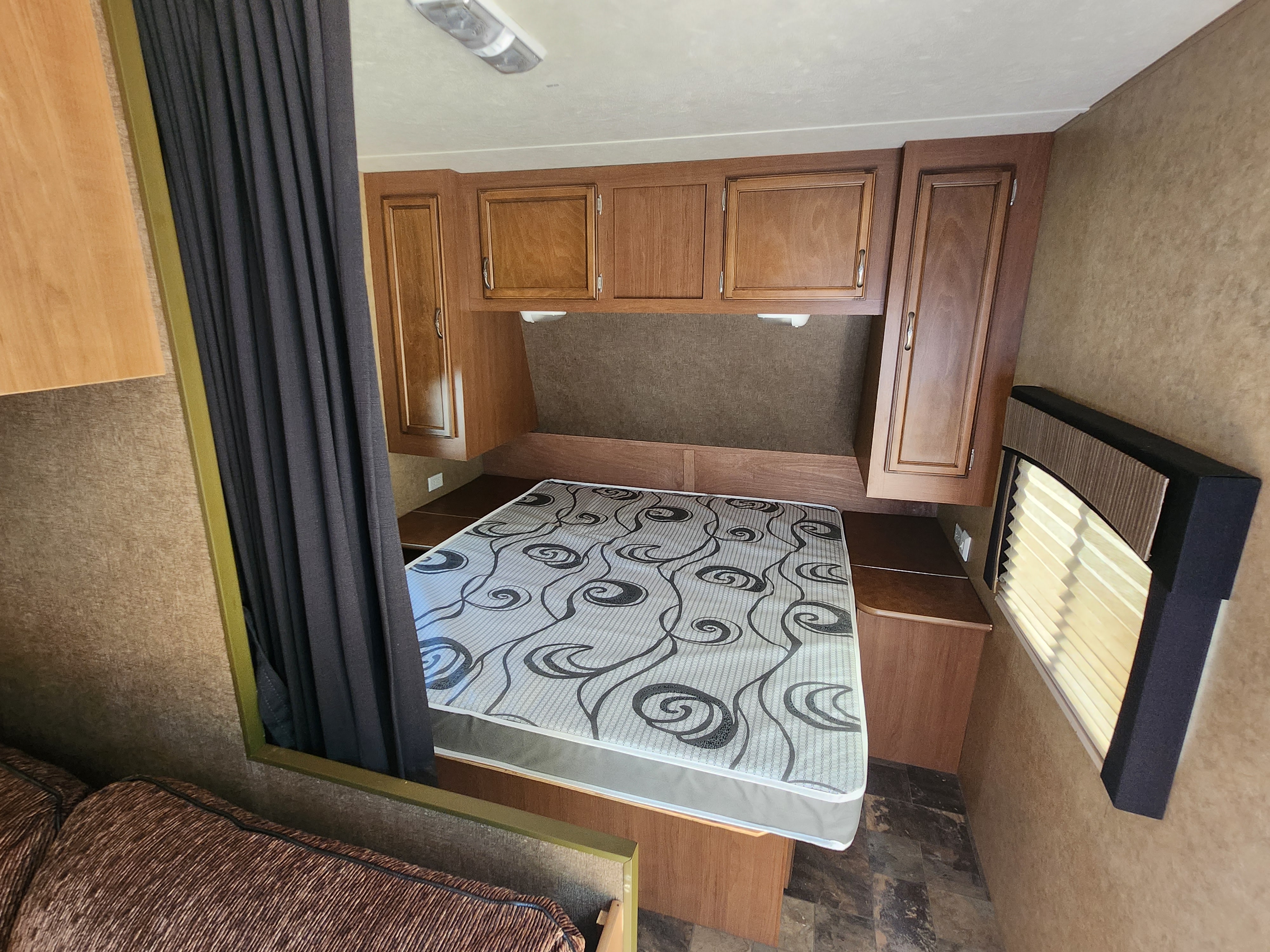 Inside a comfortable RV rental bedroom featuring a bed, wood storage cabinets, window blinds, and a privacy curtain.. Starcraft Autumn Ridge 2013