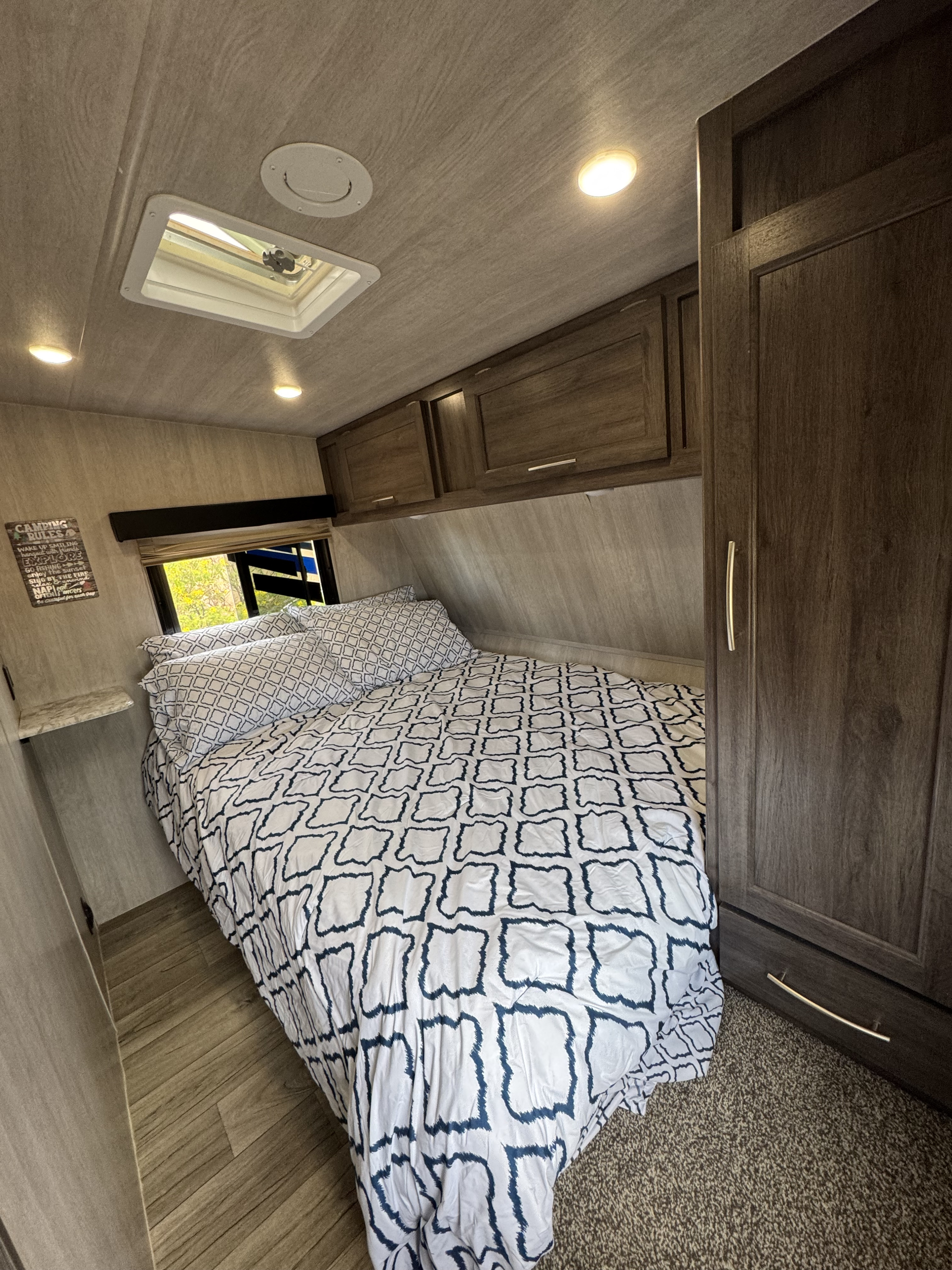 Step into this cozy RV rental bedroom. It features a patterned bed, overhead cabinets, a window, and a ceiling vent for comfort.. Genesis Supreme Rv Genesis Supreme 2023