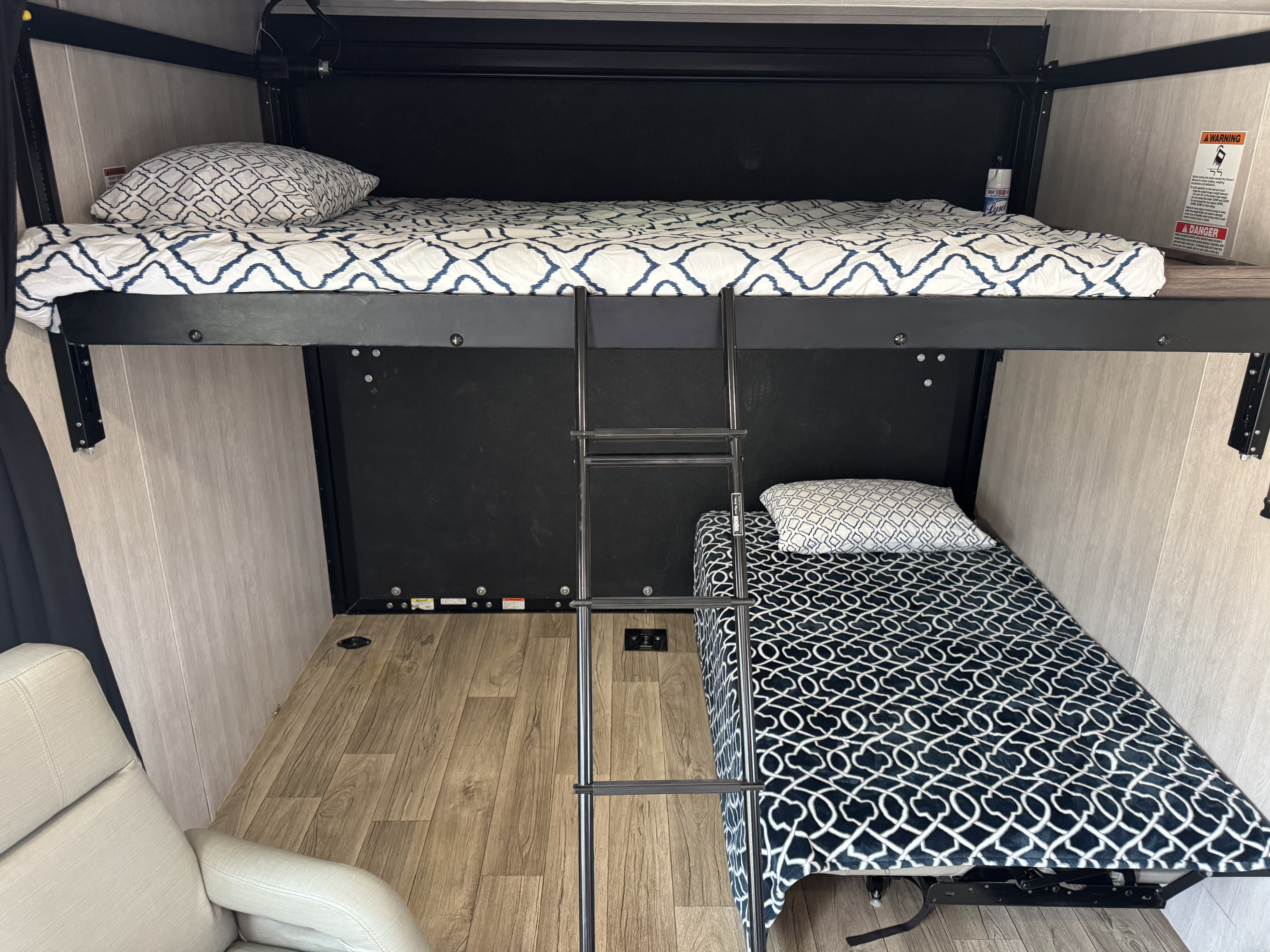 Cozy RV rental interior with bunk beds, a ladder, and a recliner. The upper bunk has a white patterned comforter.. Genesis Supreme Rv Genesis Supreme 2023