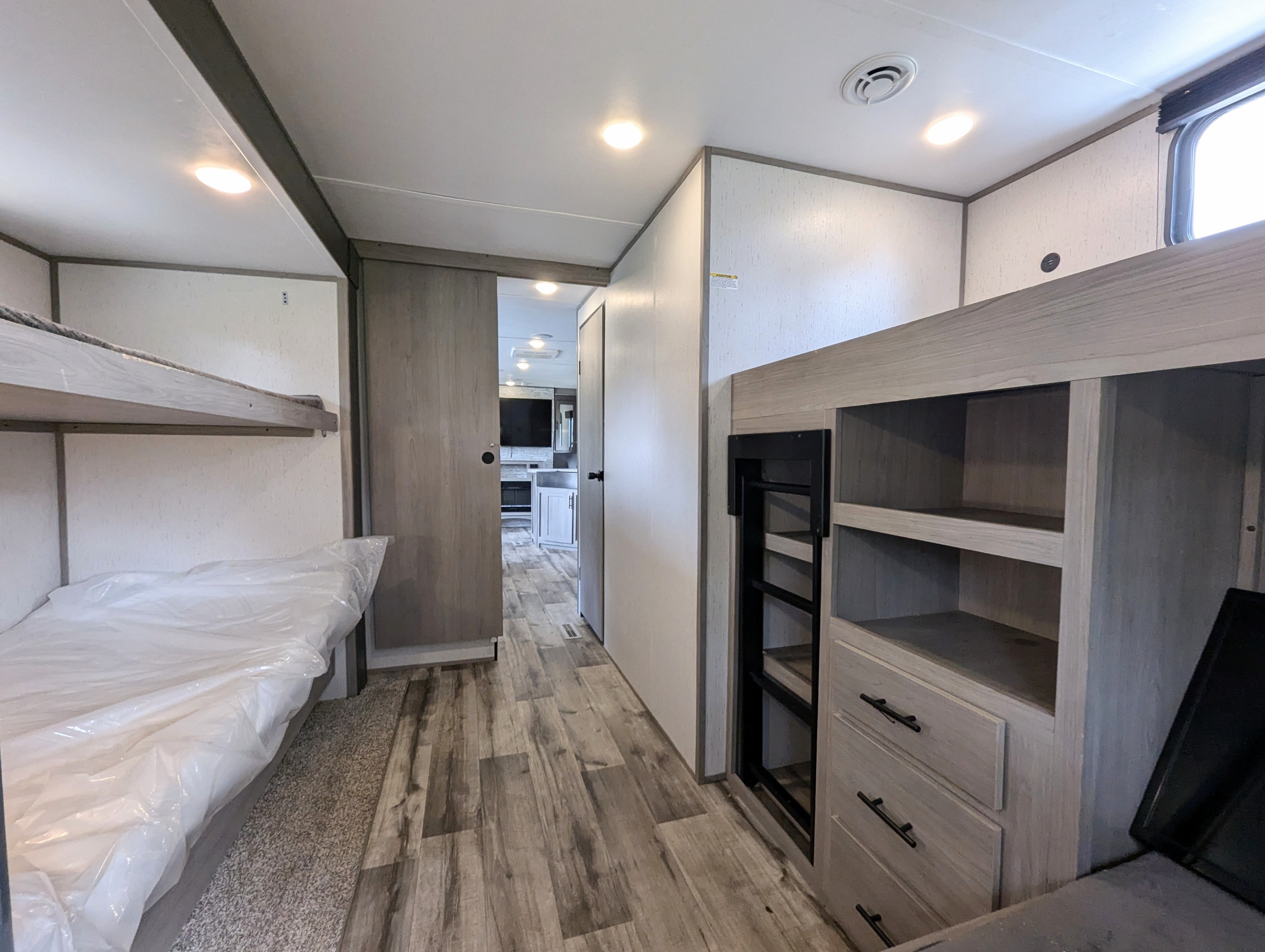 RV rental bunk area with plastic-wrapped mattresses, built-in storage, ladder, and hallway in a bright, modern interior.. Dutchmen Coleman Lantern 2022