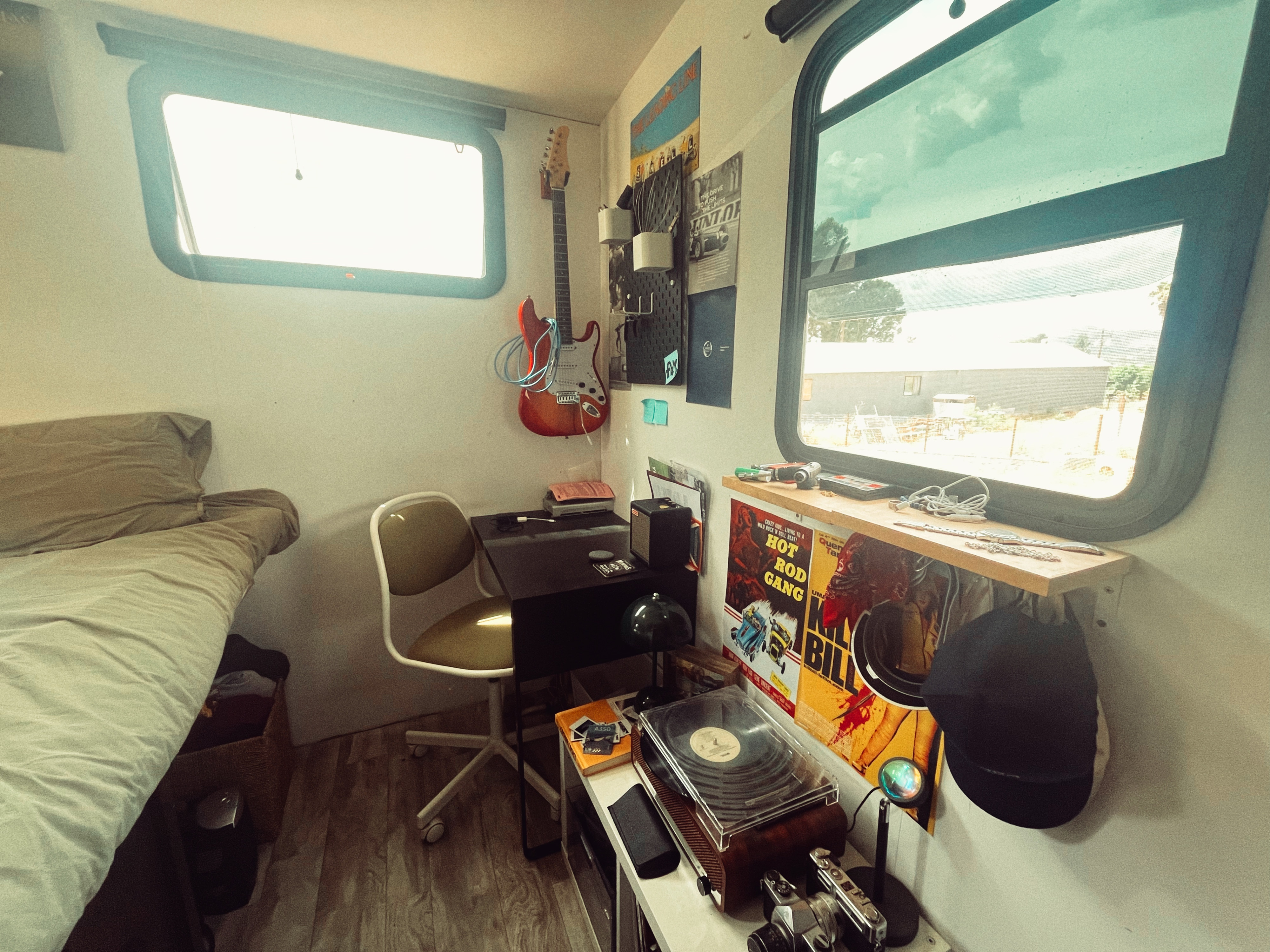 Cozy RV rental interior featuring a bed, electric guitar, desk with a chair, and a turntable with vinyl records.. Grand Design Reflection 2020
