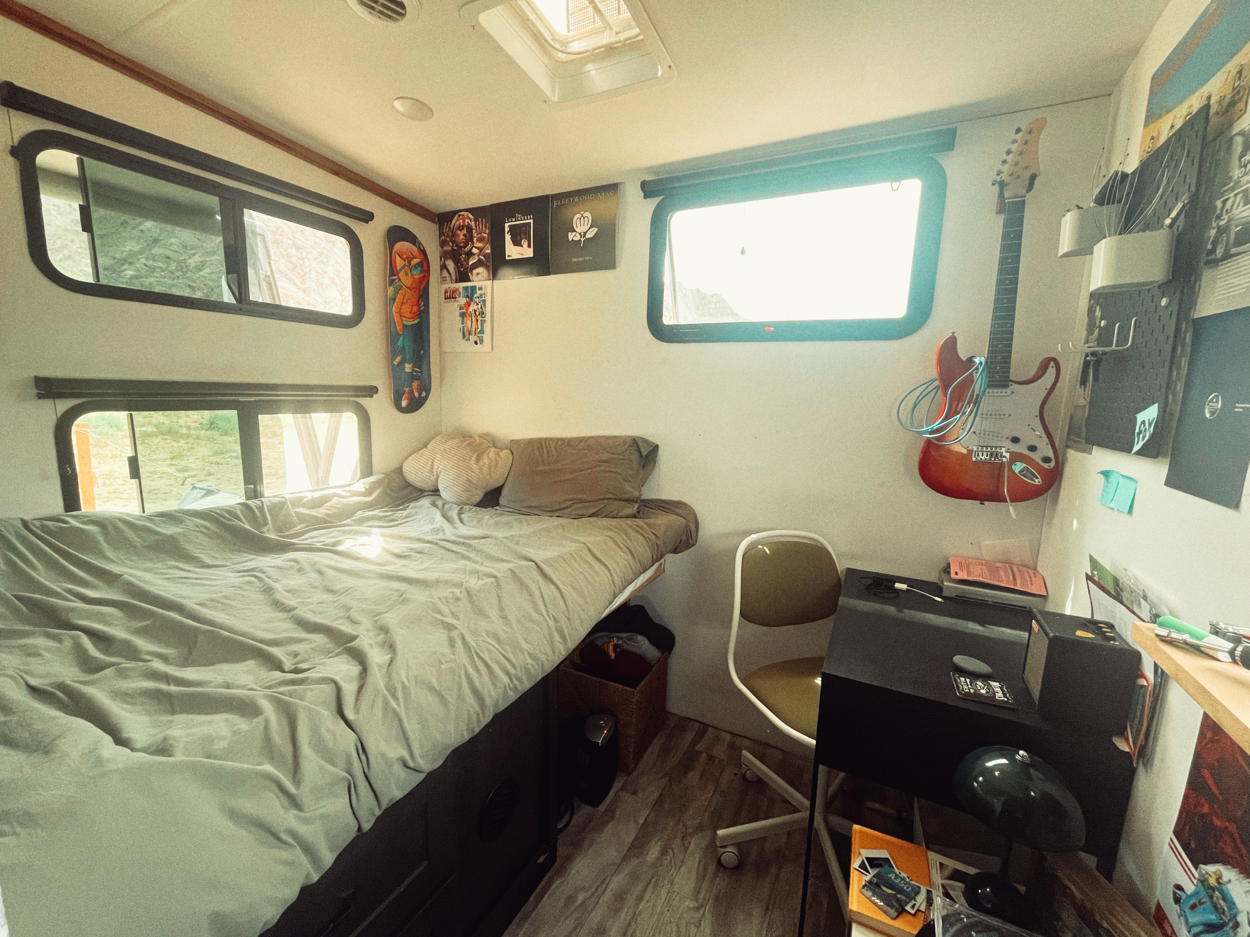 Inviting RV rental interior: bed, windows, guitar, and a compact workspace. Ideal for comfortable mobile living.. Grand Design Reflection 2020