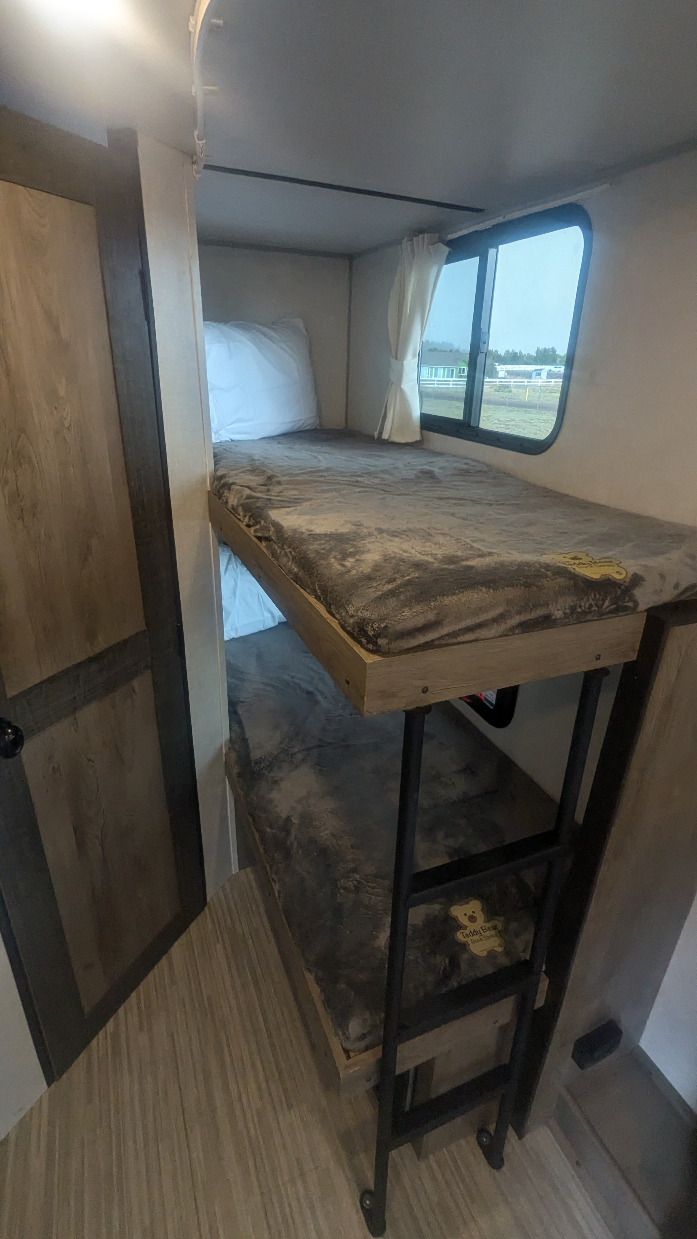 Cozy bunk beds in an RV rental, featuring plush bedding, a ladder, and a window. Ideal camper interior for family adventures.. Forest River Surveyor Legend 2021