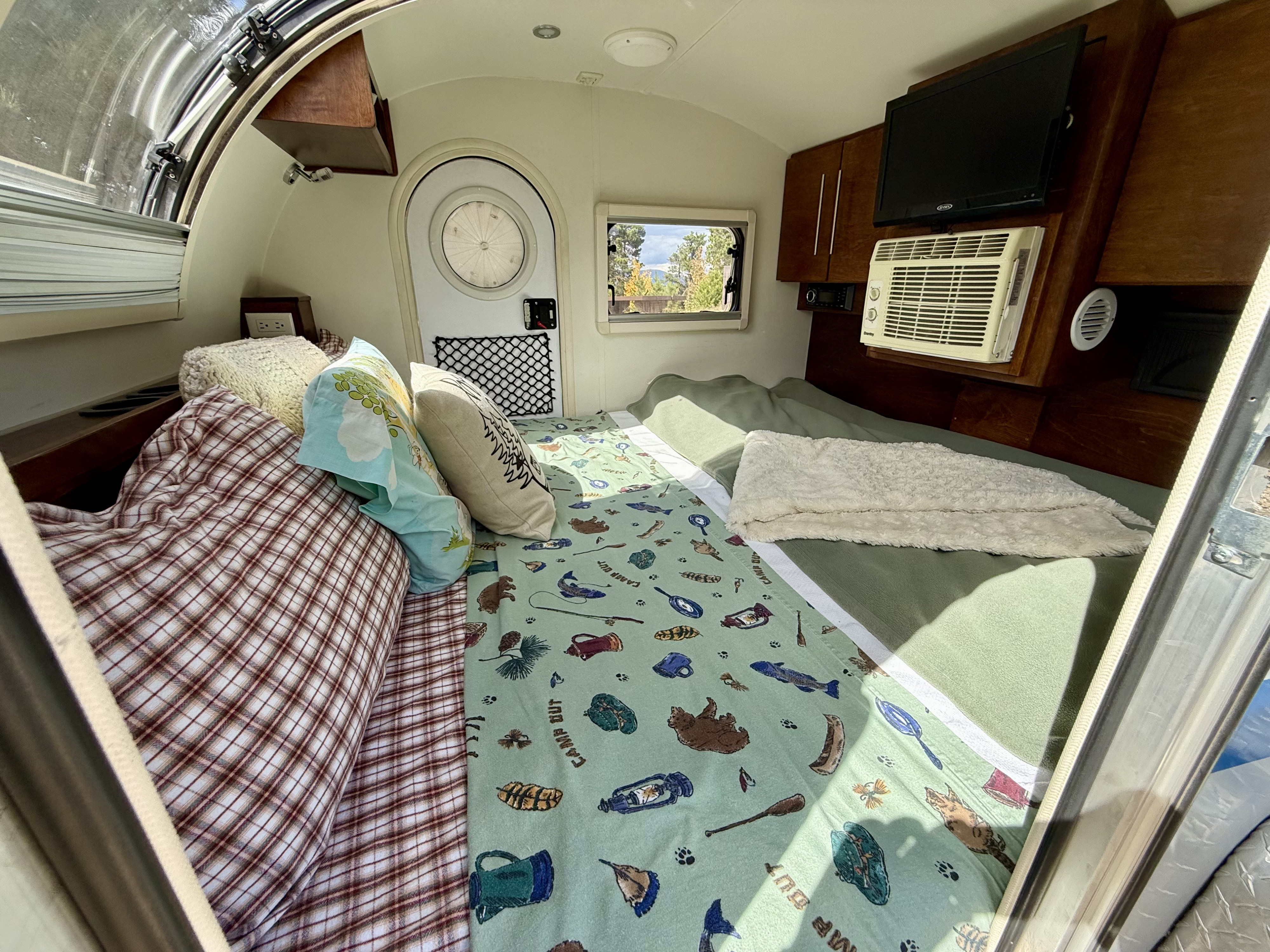 Cozy rv rental interior: comfy bed with nature-themed bedding, AC, TV, ready for your next adventure.. nuCamp T@G 2019