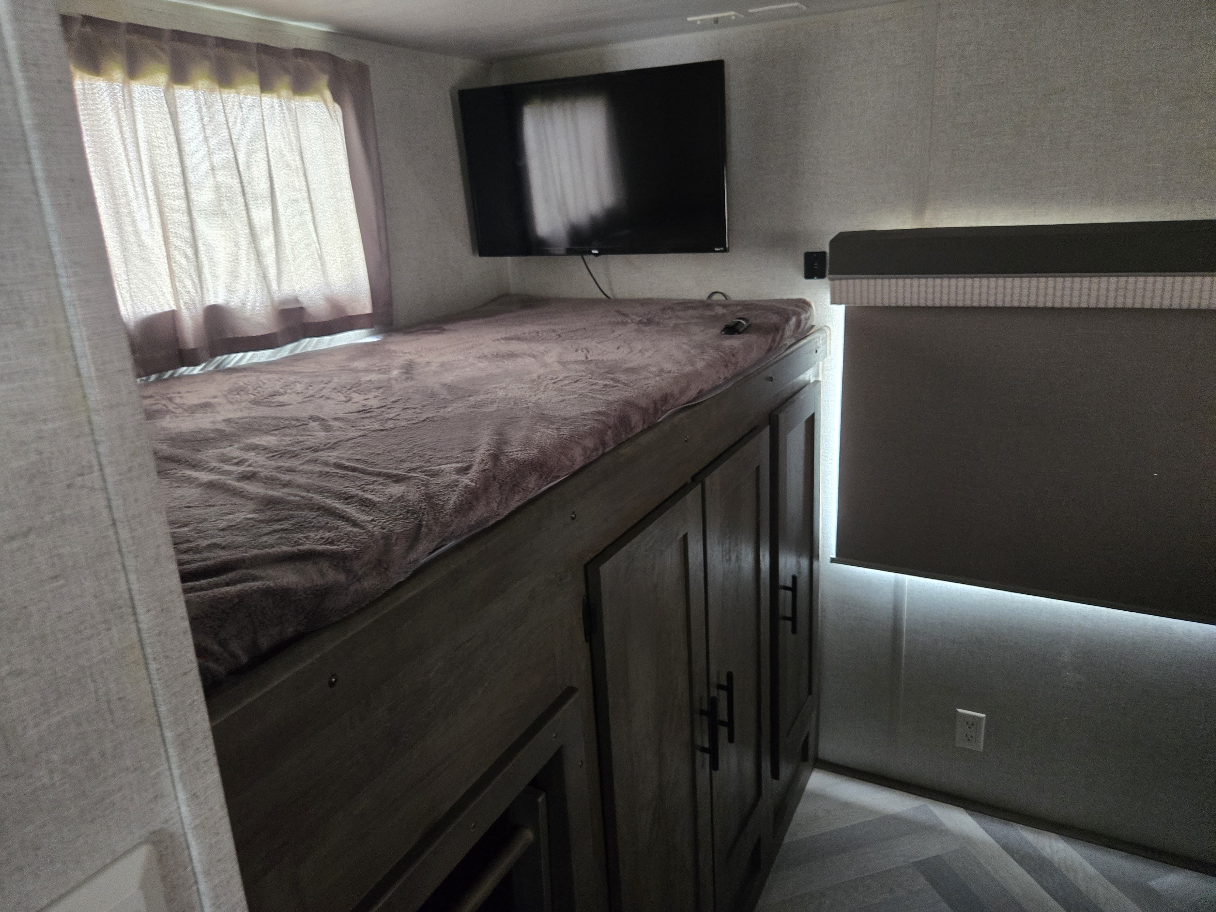 Cozy RV rental bunk bed featuring a TV, window with curtains, and built-in cabinets below, all in a compact interior.. Forest River Salem 2021
