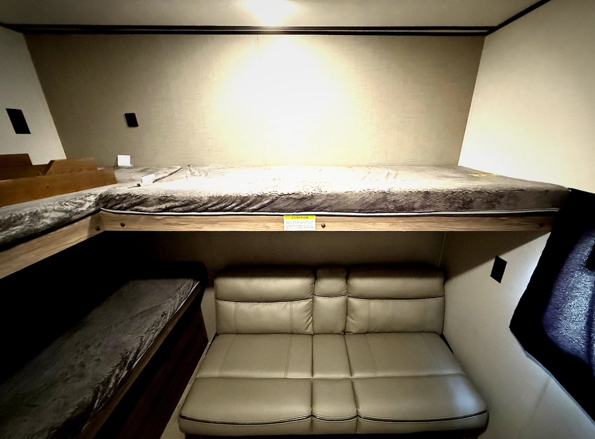An RV rental's cozy interior featuring bunk beds stacked above a comfortable sofa, perfect for family adventures.. Crossroads RV Zinger 2024