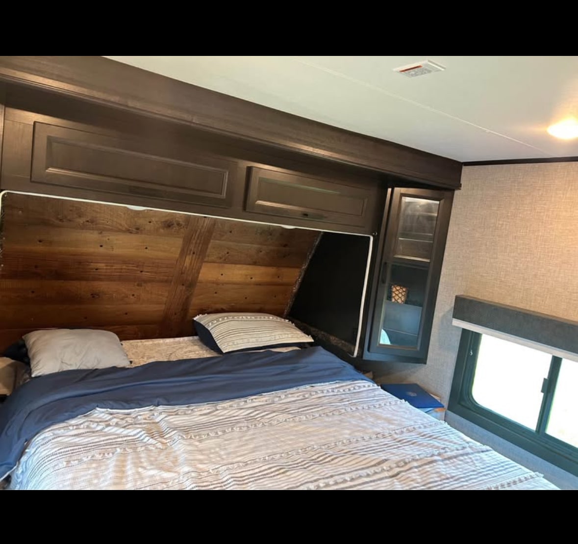 Cozy RV rental bedroom with a rustic wooden headboard, dark overhead cabinets, and a comfortable blue and white striped bed.. Jayco Eagle HT 2022