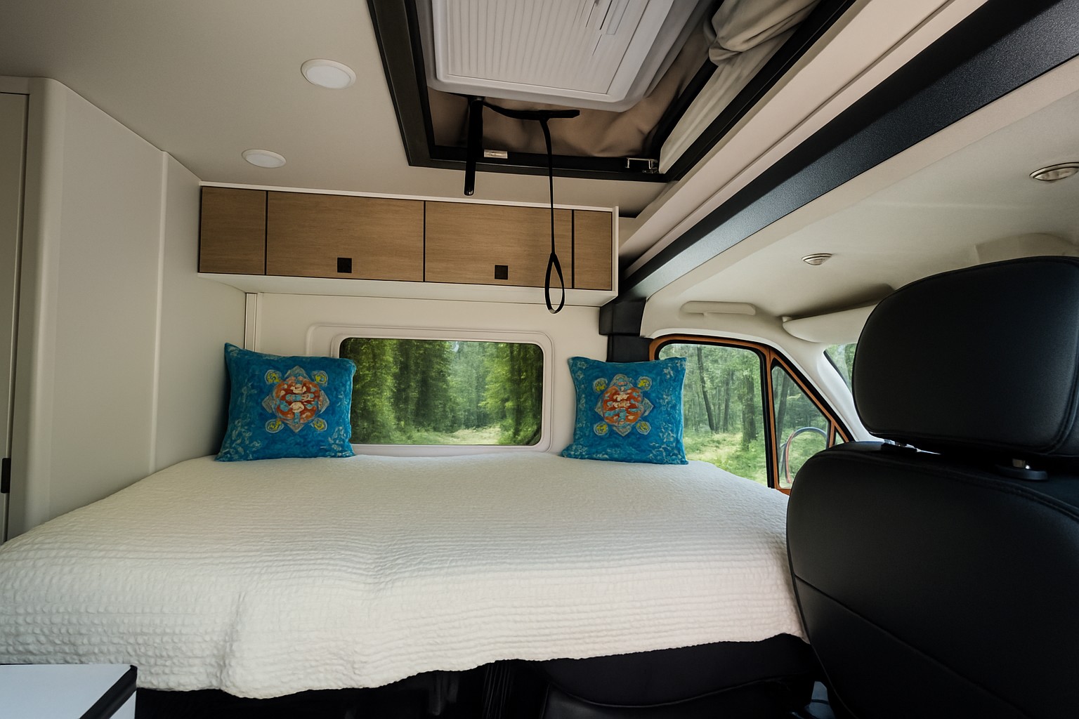 This comfortable RV rental features a cozy bed with colorful pillows, offering a scenic forest view for your adventures.. Ram Wave Pop Top 2025