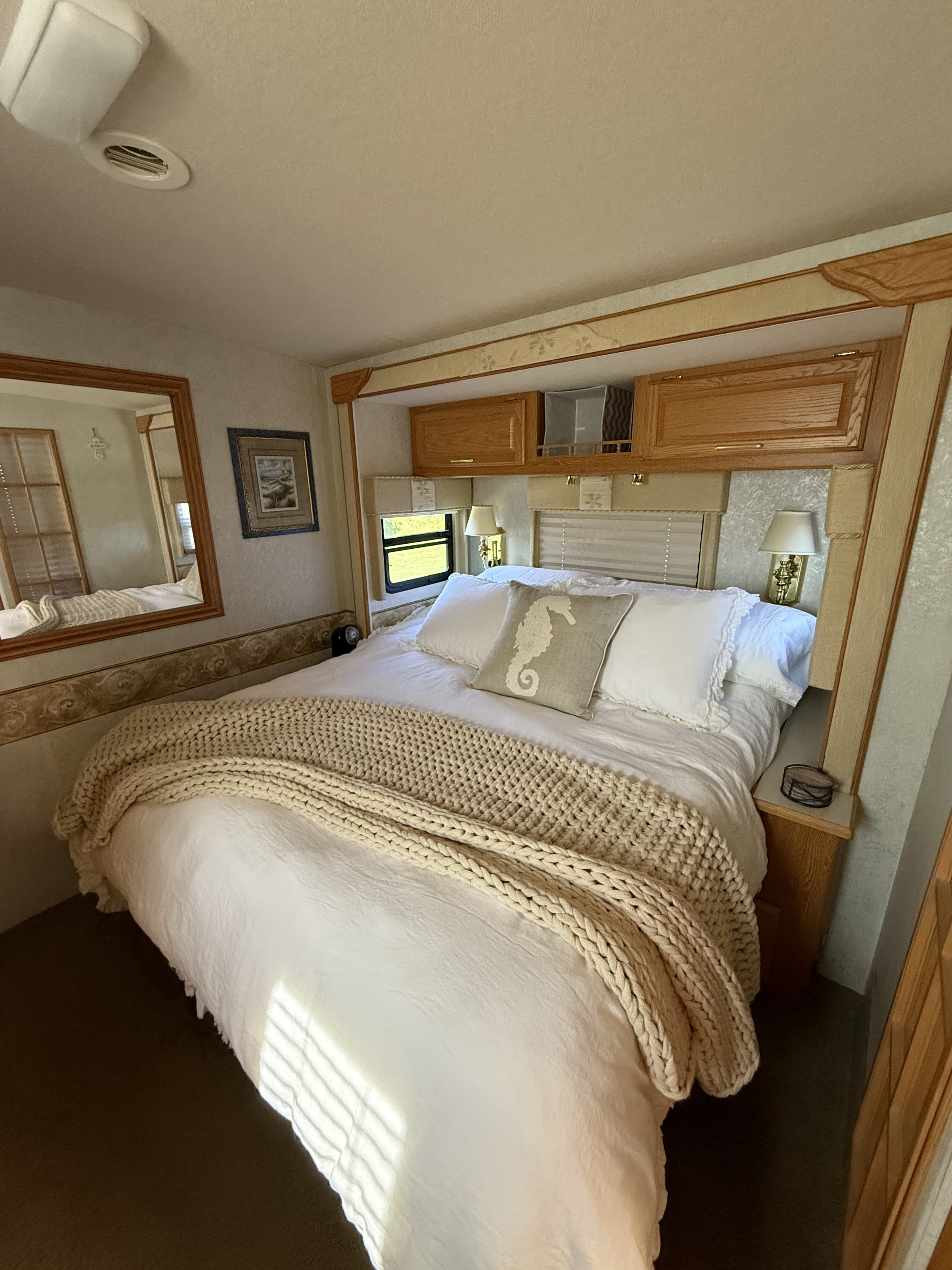 Comfortable RV rental bedroom featuring a bed with white linens, a knit throw, and warm wood accents.. Winnebago Adventurer 2005