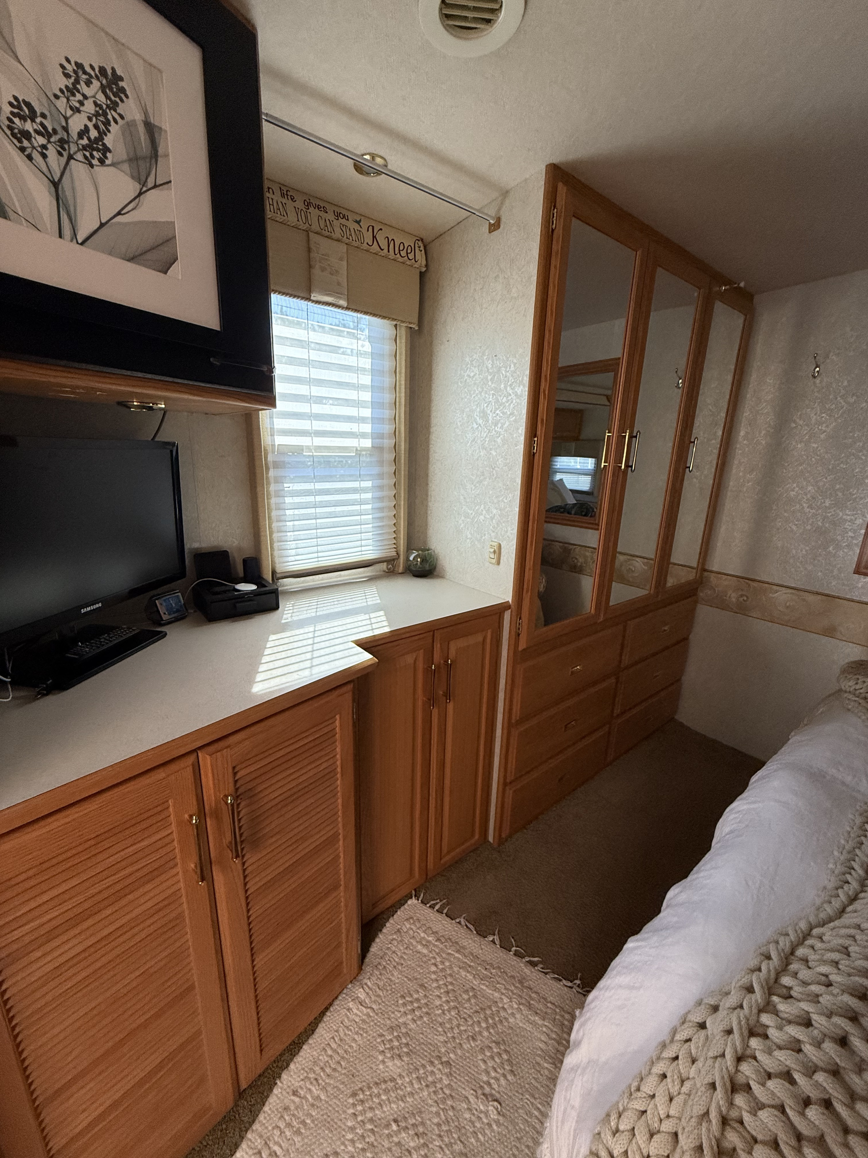 Cozy RV rental bedroom featuring a desk, TV, window, and ample mirrored wardrobe storage for mobile living.. Winnebago Adventurer 2005