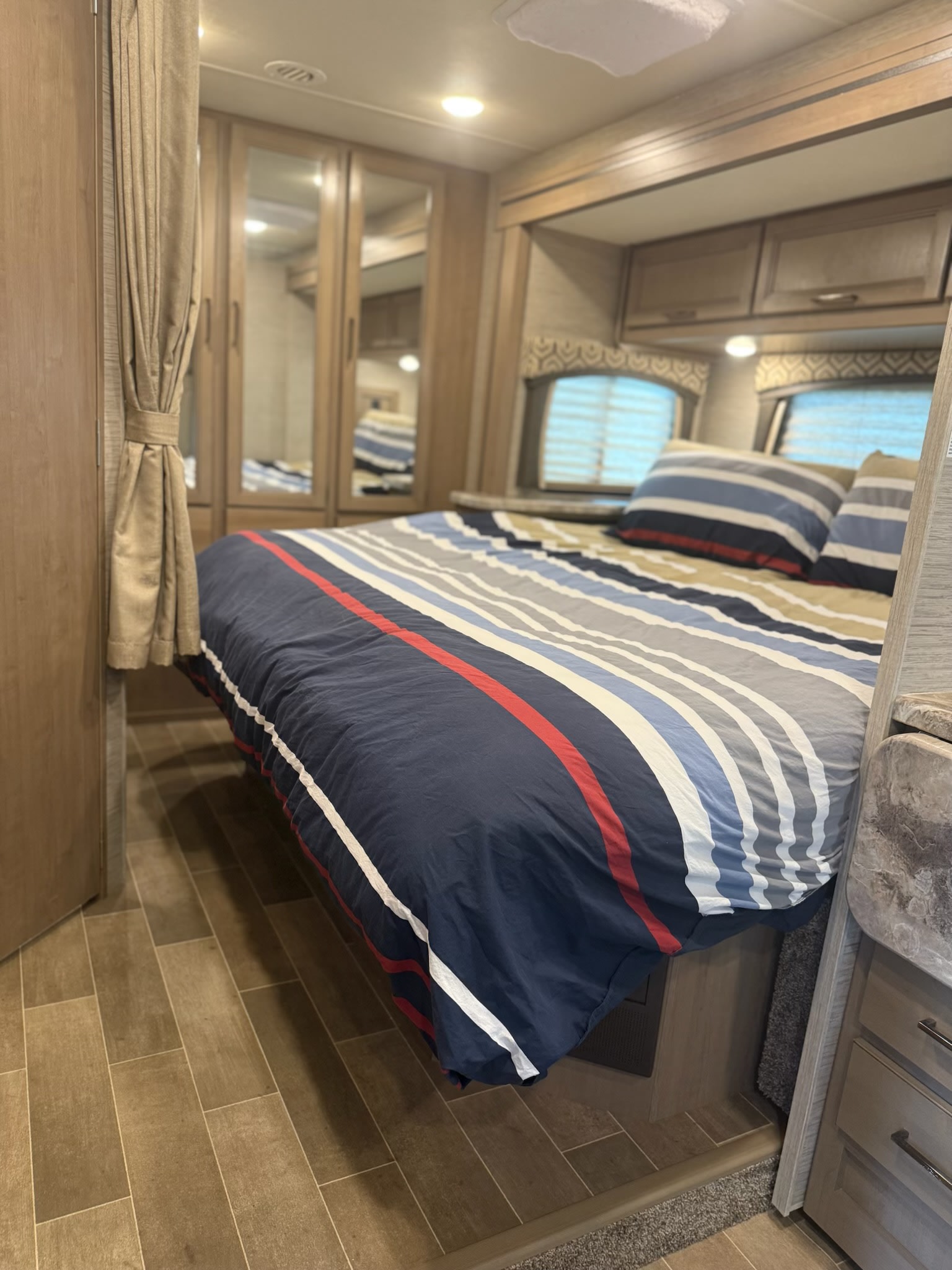 This RV rental bedroom features a striped bed, mirrored closet, and warm wood tones for a cozy interior.. Thor Chateau 2021