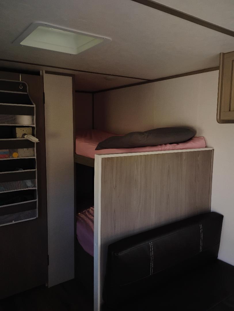 RV rental: A compact bunk bed area with pink bedding, a black sofa, hanging storage, and a ceiling vent.. Dutchmen Coleman 17B 2024