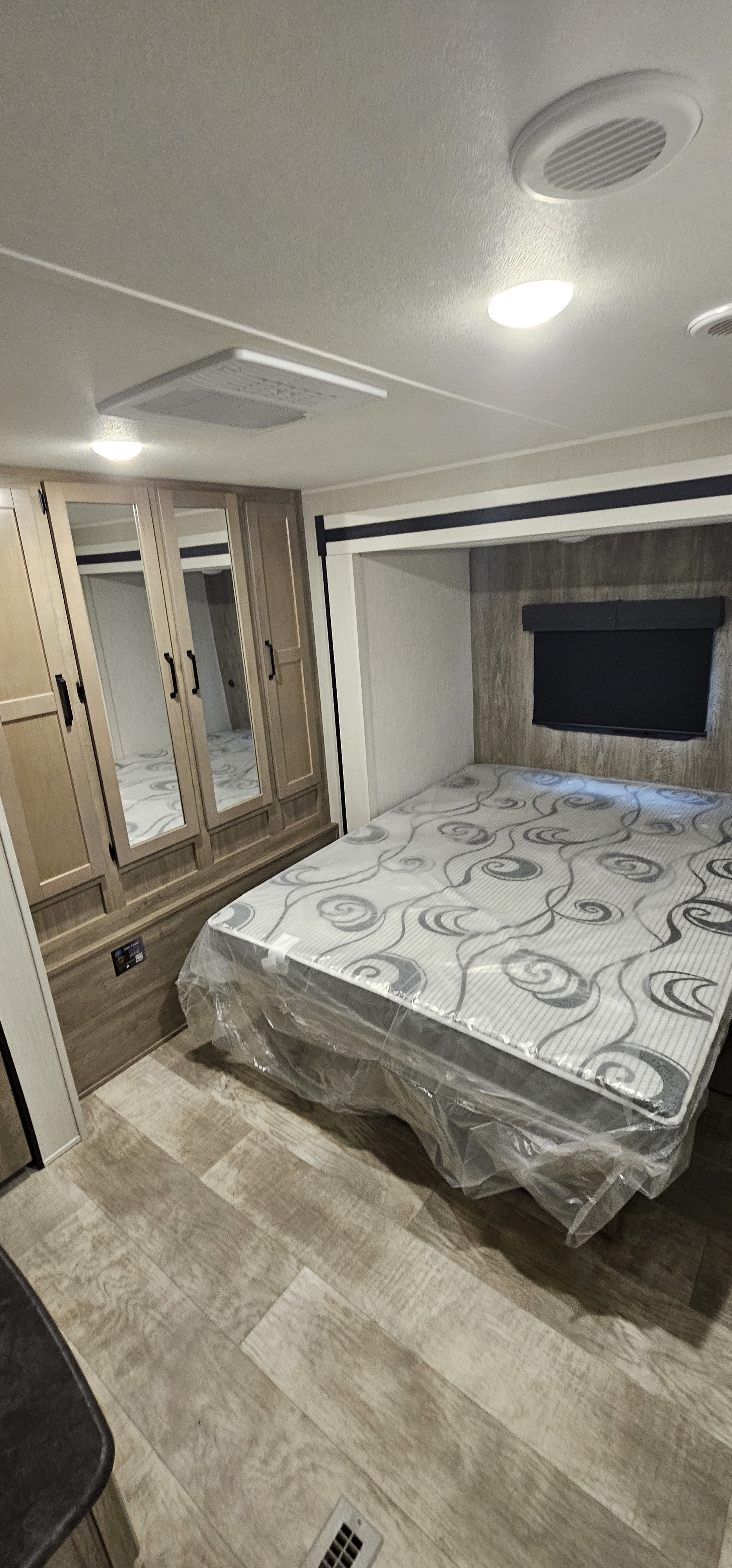 Clean RV rental bedroom featuring a new, plastic-wrapped mattress, mirrored wardrobes, and wood-look flooring.. Forest River Palomino Puma 2024