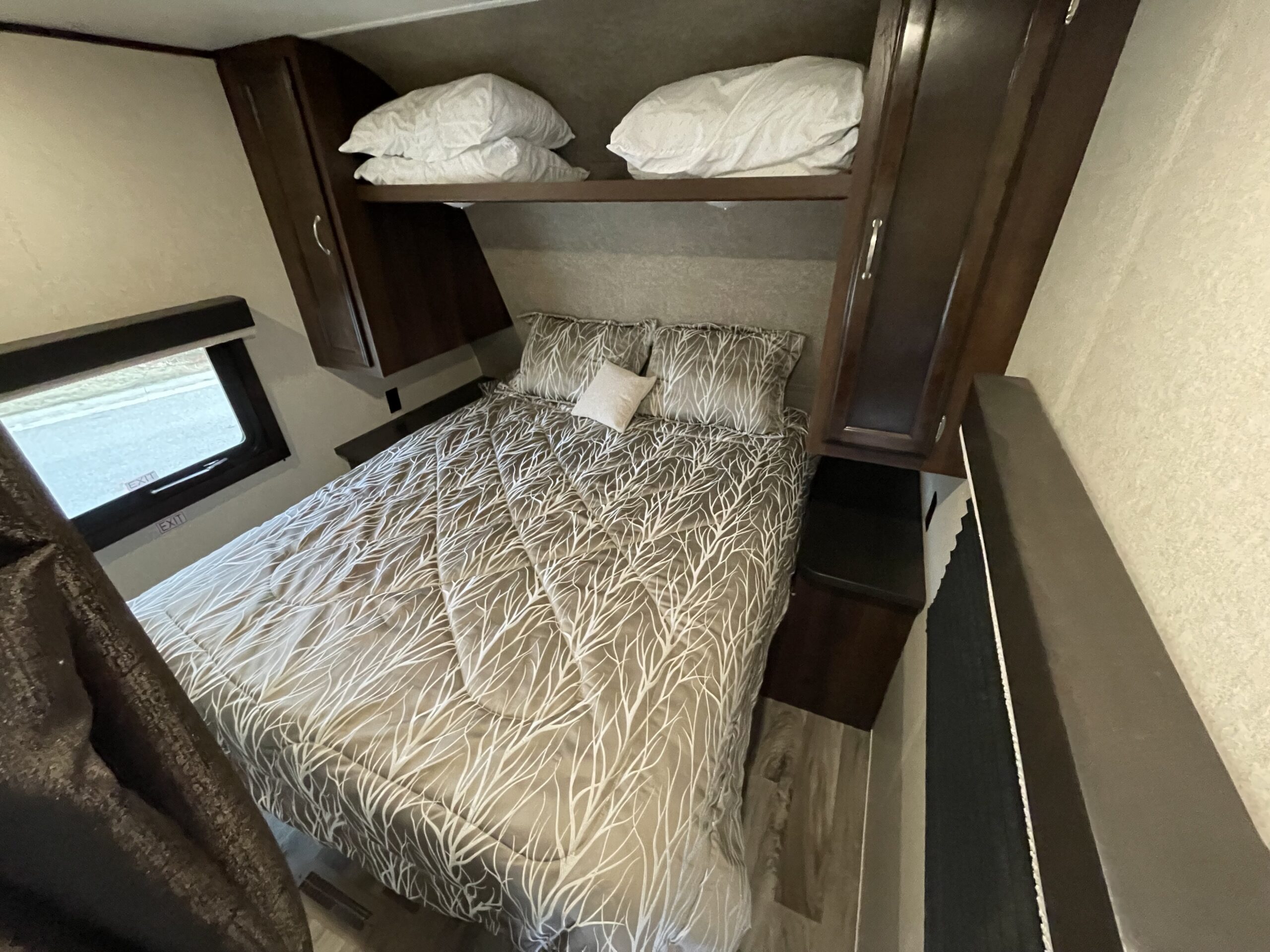 Cozy rv rental bedroom with patterned bedding, overhead storage cabinets, and an emergency exit window.. Jayco Jayflight 2018