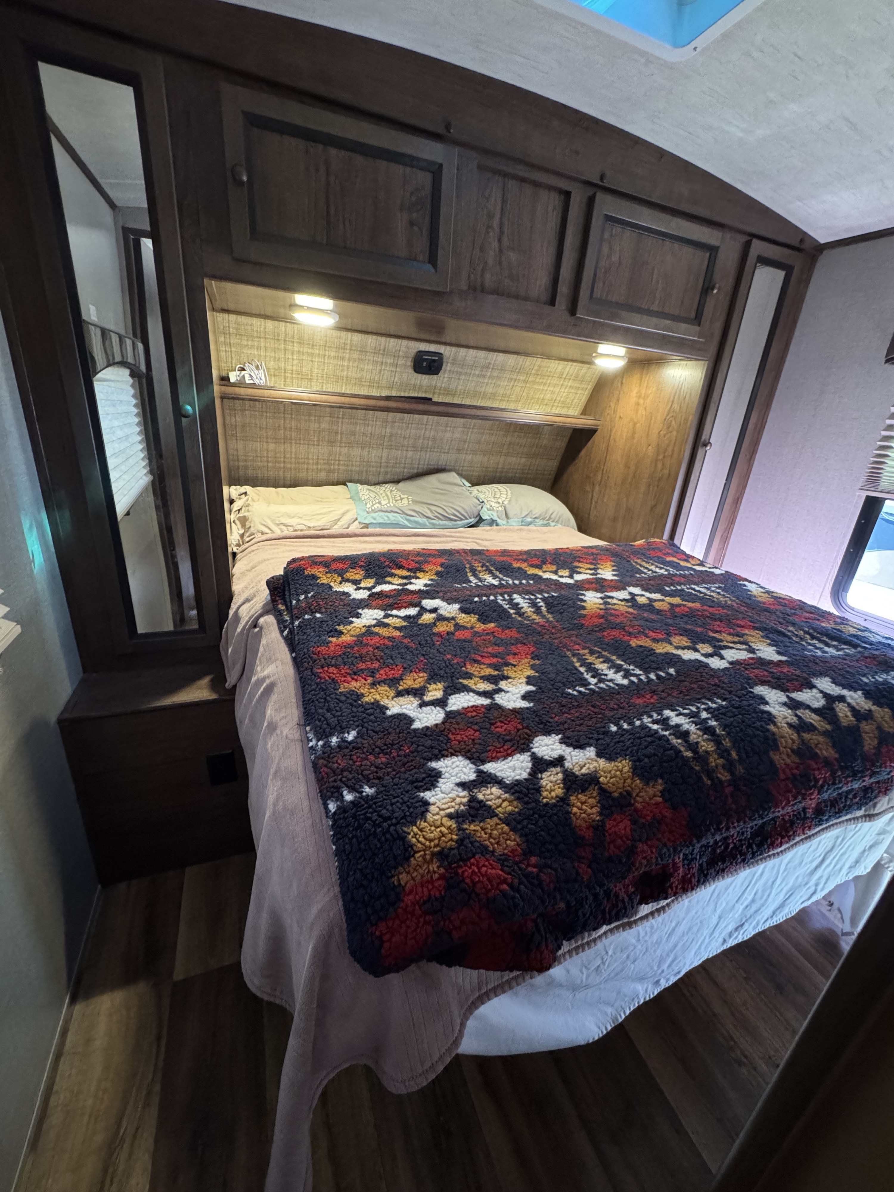 Cozy RV rental bedroom features a comfortable bed with a vibrant blanket, built-in storage, and reading lights.. Cruiser RV MPG Ultra Lite 2017
