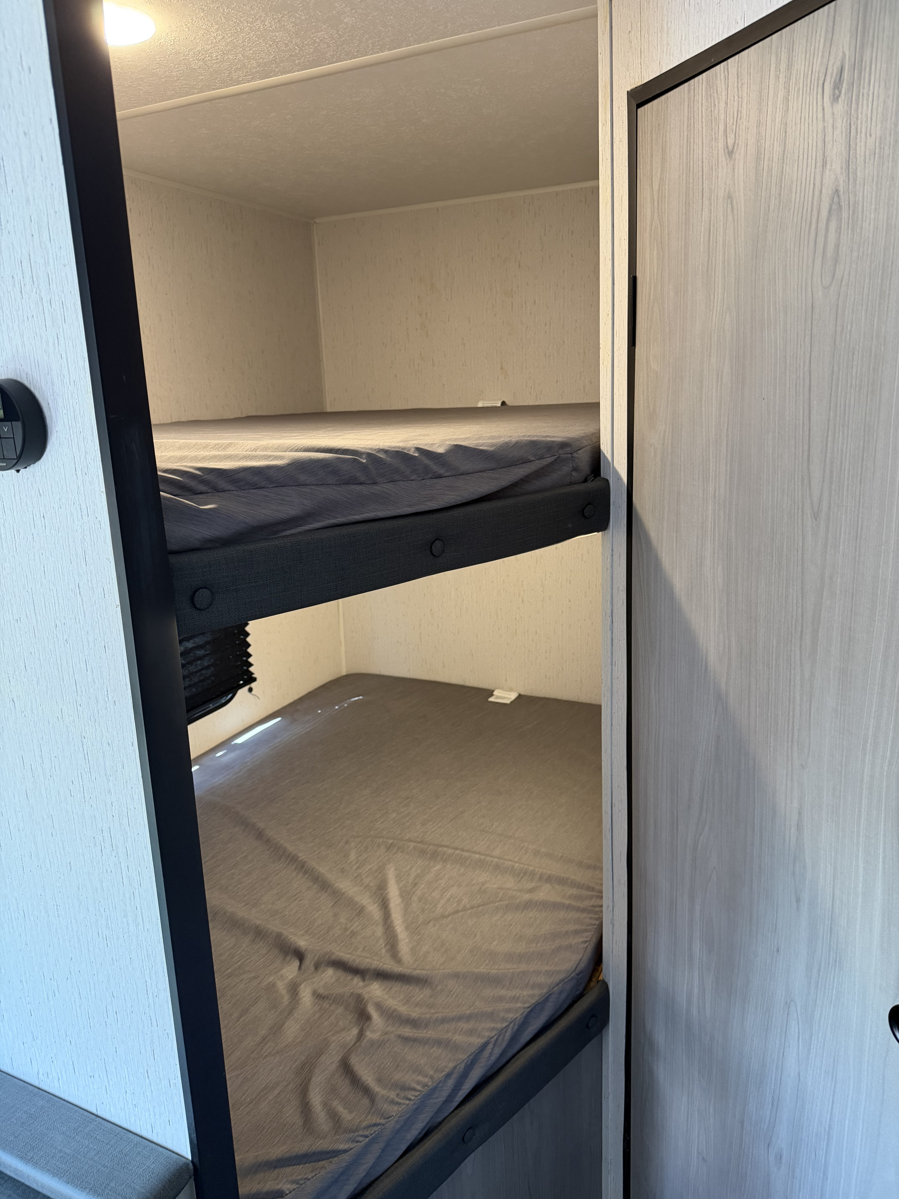 Compact RV rental bunk beds with grey sheets, offering a practical sleep area within a light-toned interior.. Dutchmen Coleman Lantern LT - 274BHWE 2024