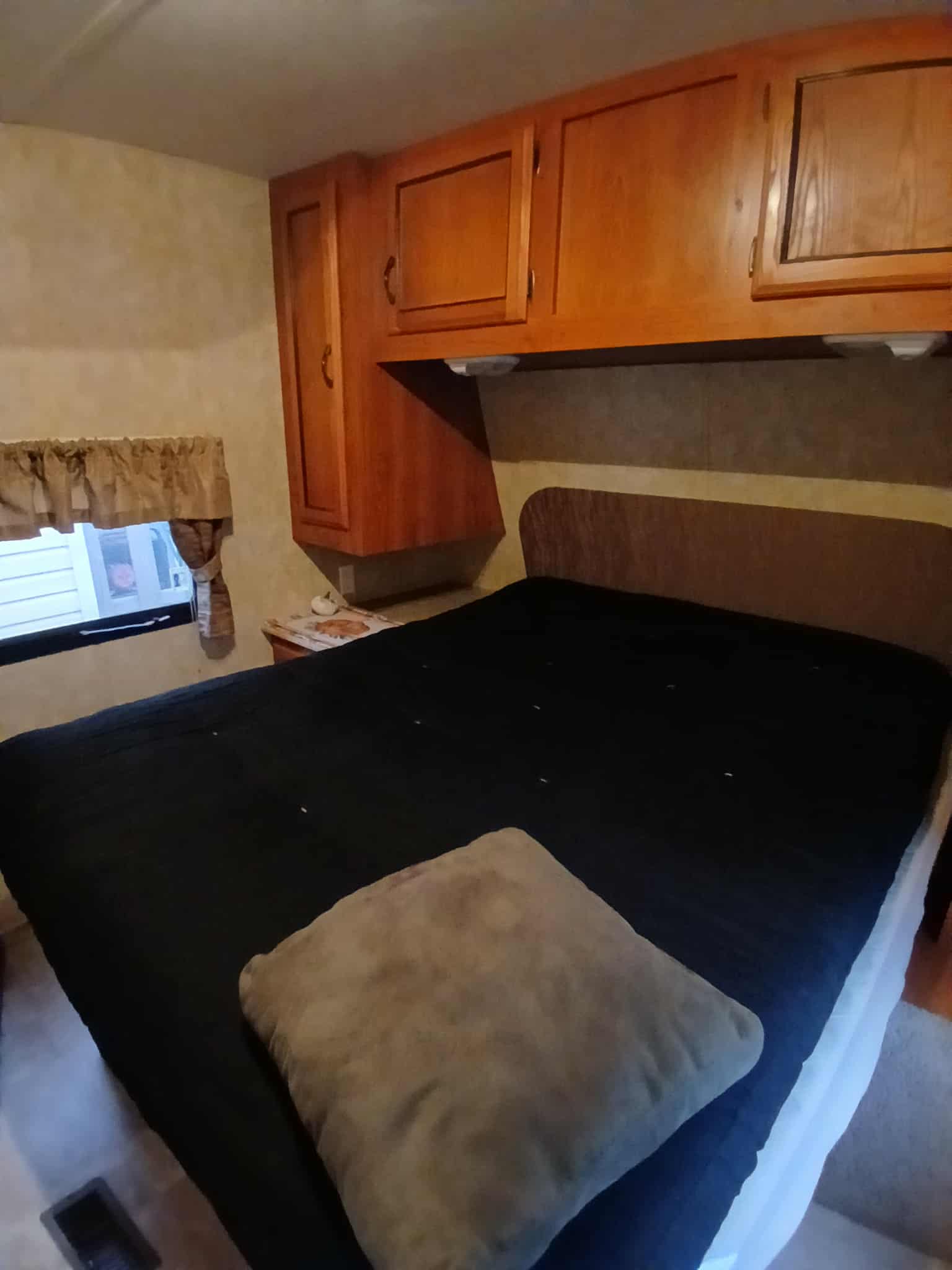 Inside an **rv rental** bedroom: a bed with black bedding, wood cabinets, and a window with drapes.. Forest River Coachmen Catalina 2011