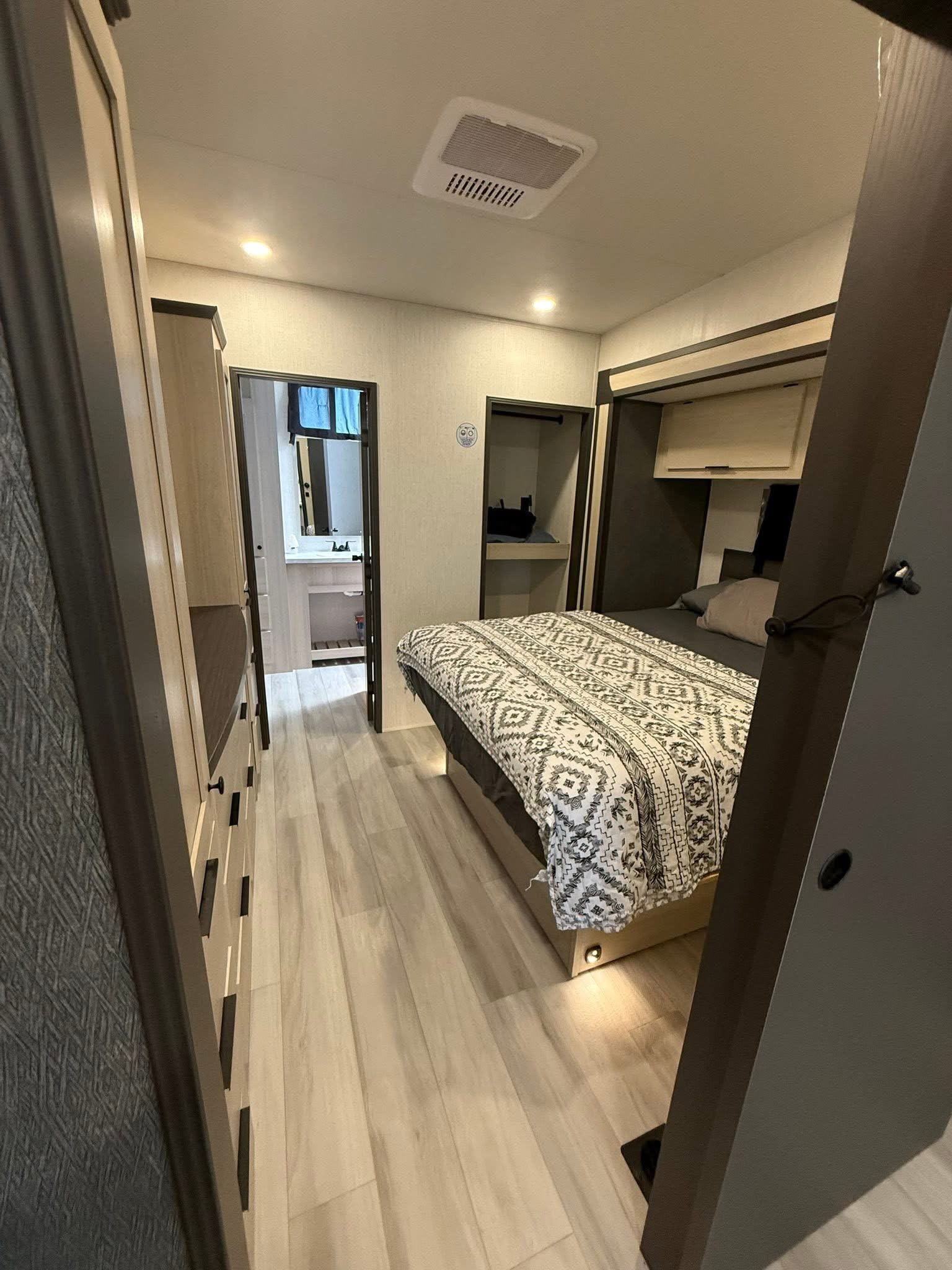 Cozy RV rental bedroom with a modern bed, dresser, and a glimpse of the bathroom. Well-lit interior.. Forest River Cardinal 2025