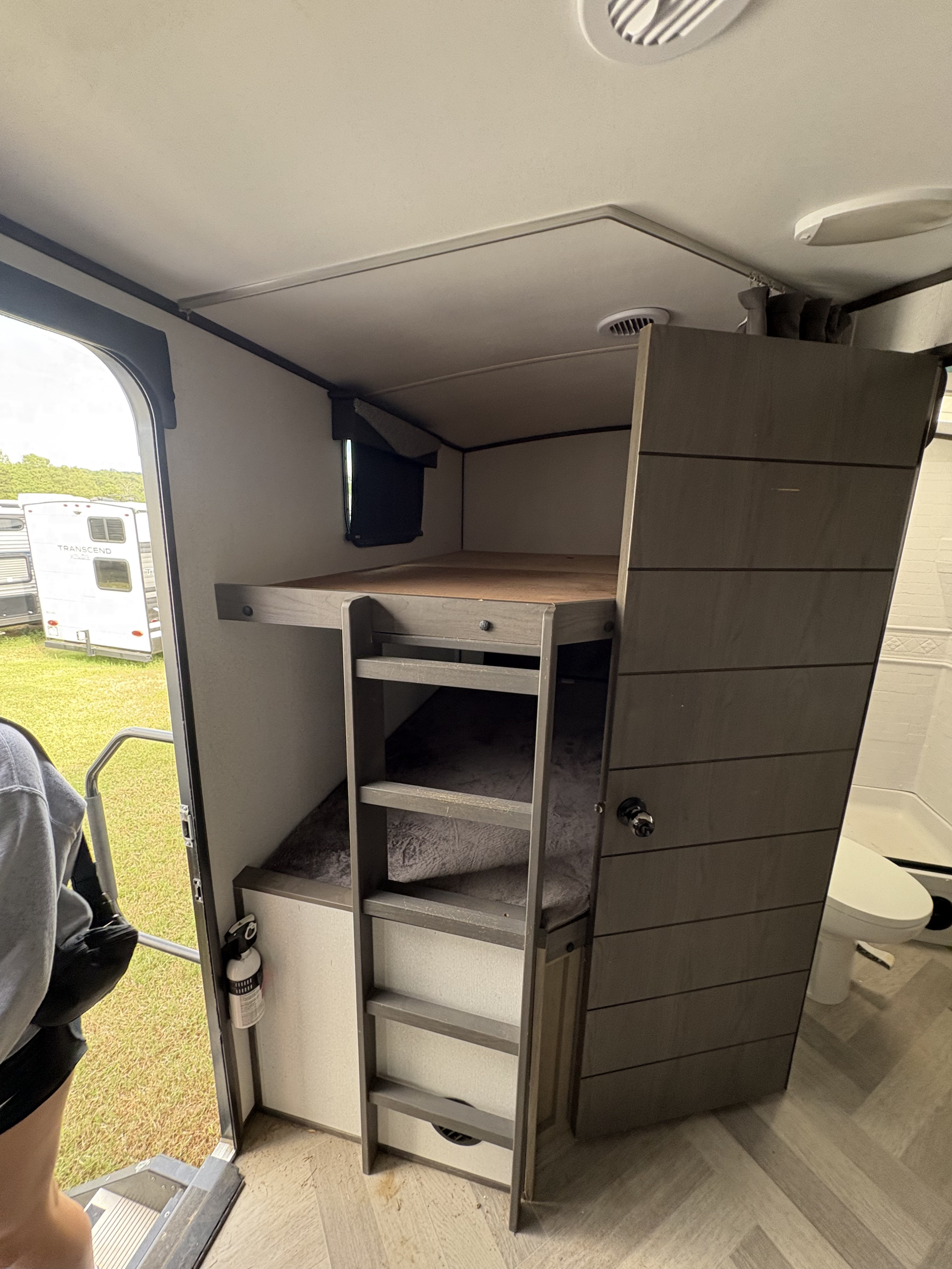 Inside an RV rental: functional bunk beds with ladder, a safety fire extinguisher, and a peek at the bathroom.. Cruiser RV Twilight 2021