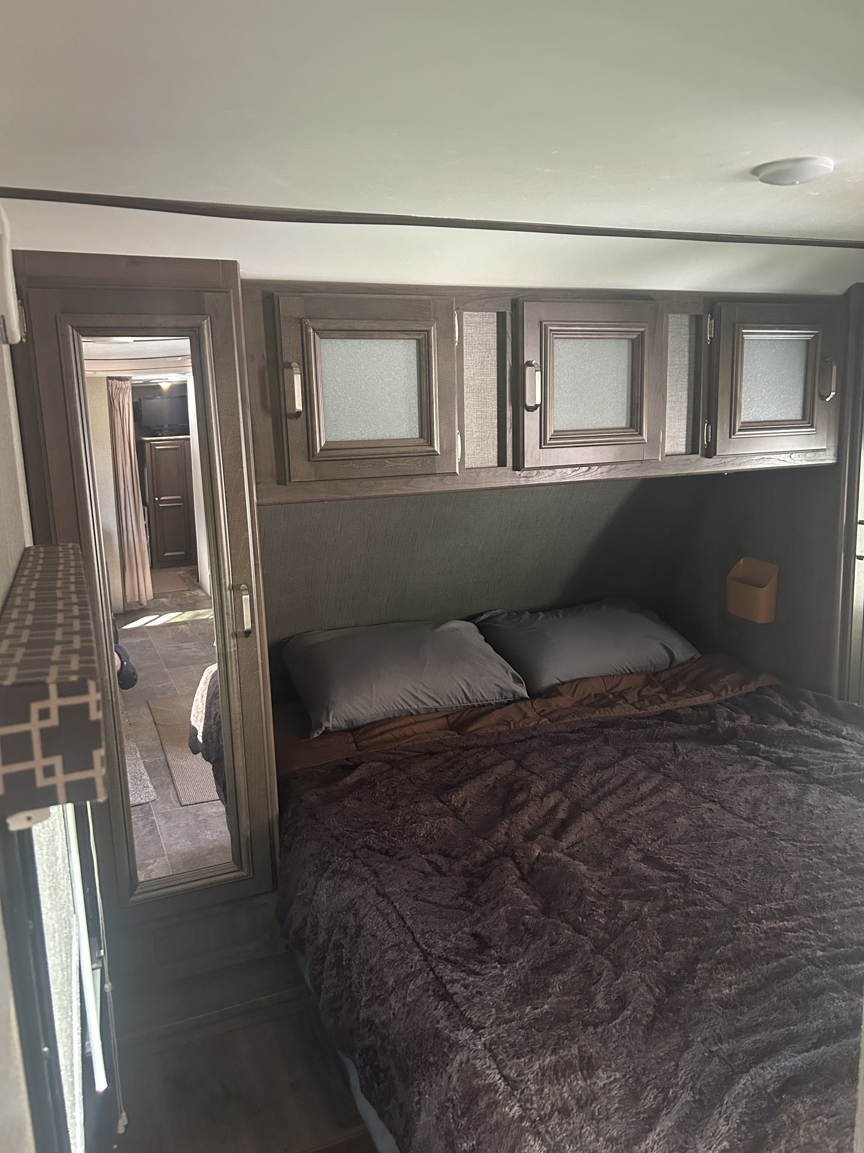 Cozy RV rental bedroom: plush bed, dark wood cabinets, and a mirrored door reflecting the interior.. Keystone Passport 3350BH 2018