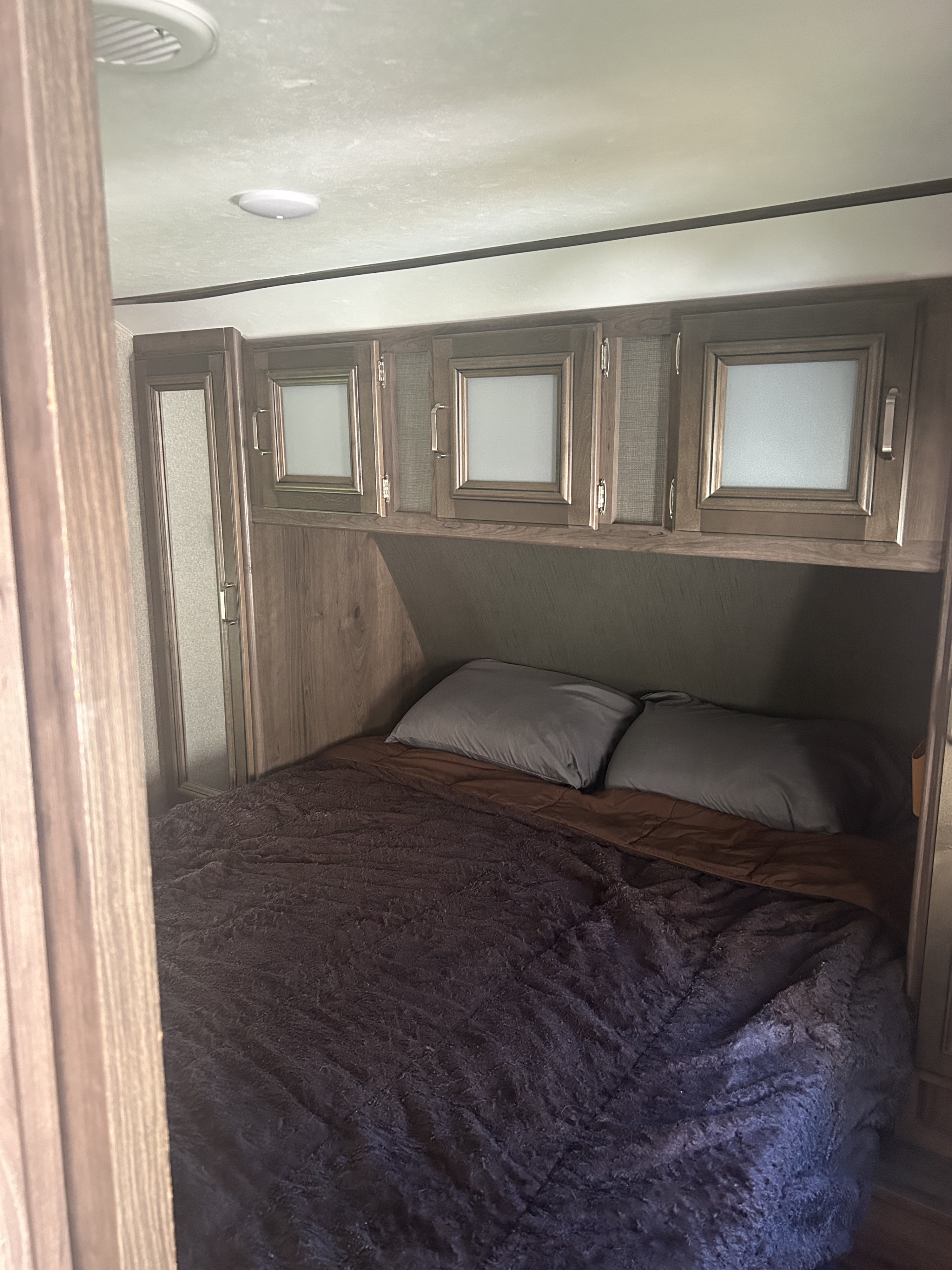 Compact RV rental bedroom featuring a dark bed, gray pillows, and practical overhead storage cabinets.. Keystone Passport 3350BH 2018