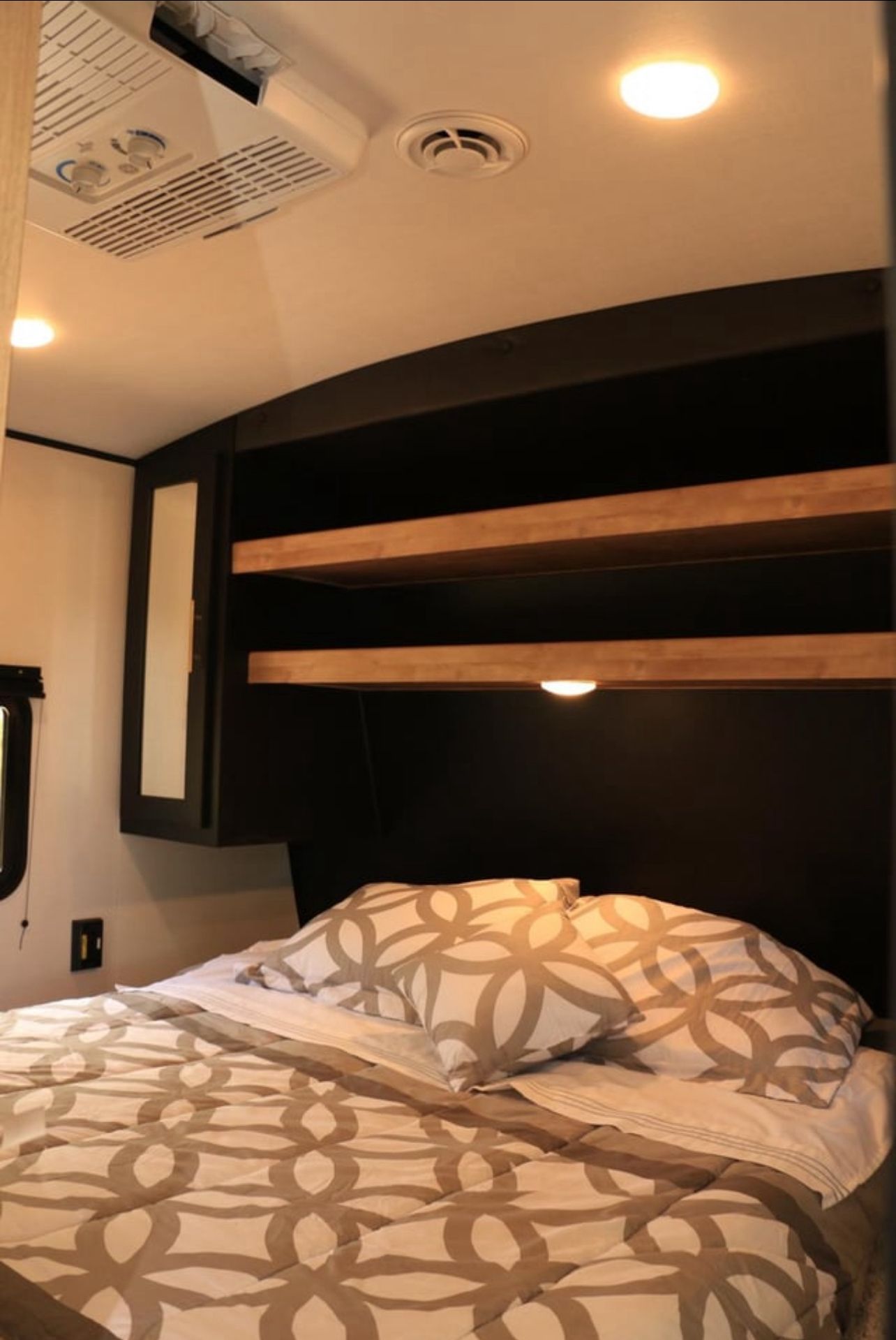 Inviting RV rental bedroom features a cozy bed with patterned linens, overhead storage, and an AC unit for comfortable travel.. Keystone RV Springdale 2022