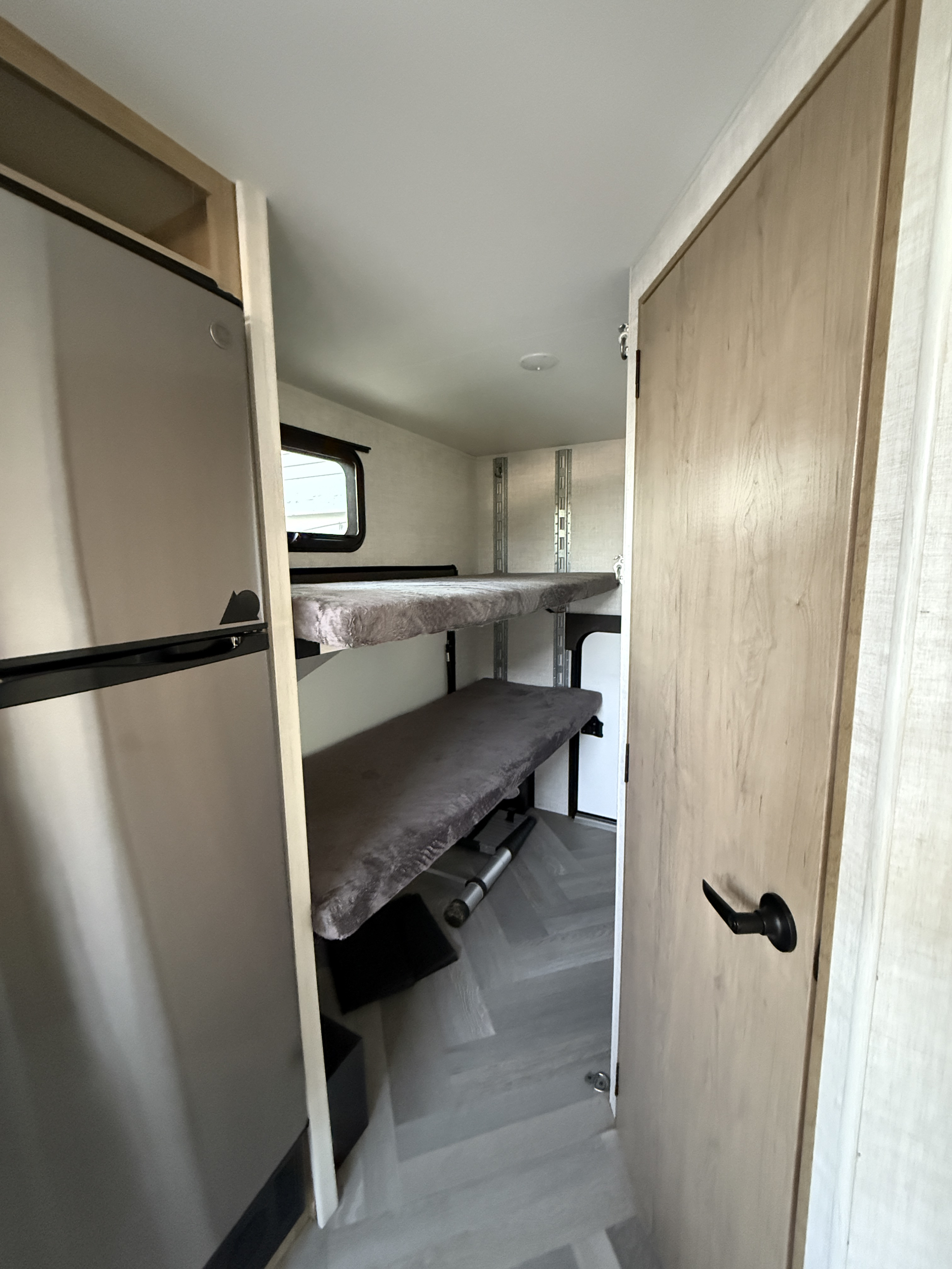 Compact RV rental interior featuring a refrigerator, bunk beds, and a door, ideal for family travel.. Ember Overland 2022