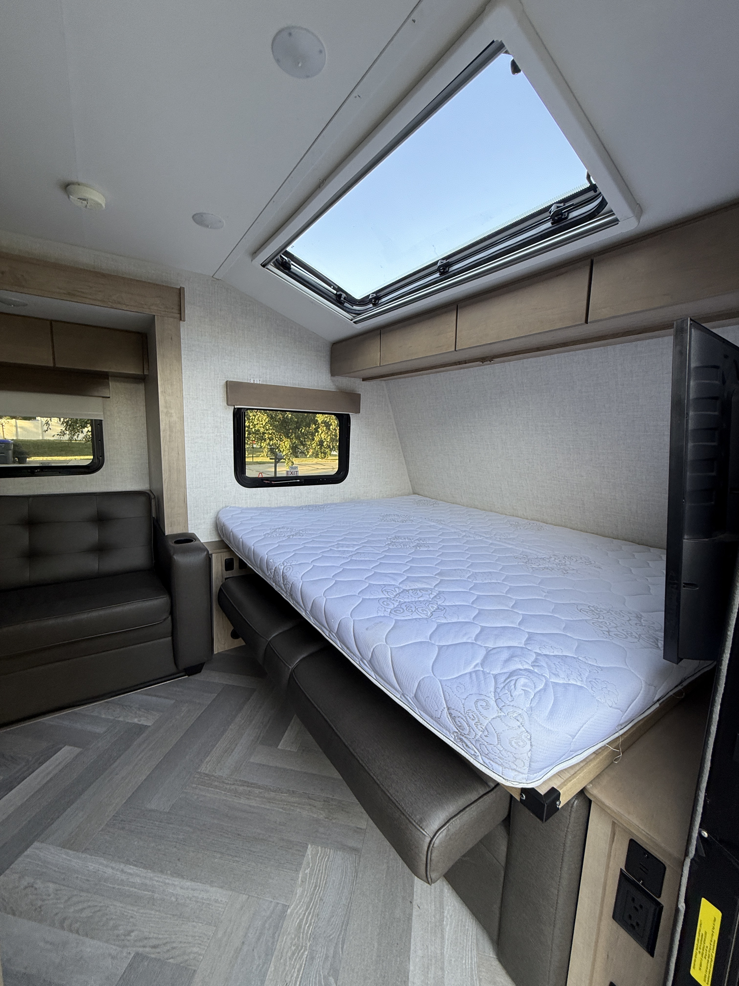 Bright RV rental interior featuring a cozy bed, sofa, overhead skylight, storage cabinets, and herringbone flooring for travel comfort.. Ember Overland 2022