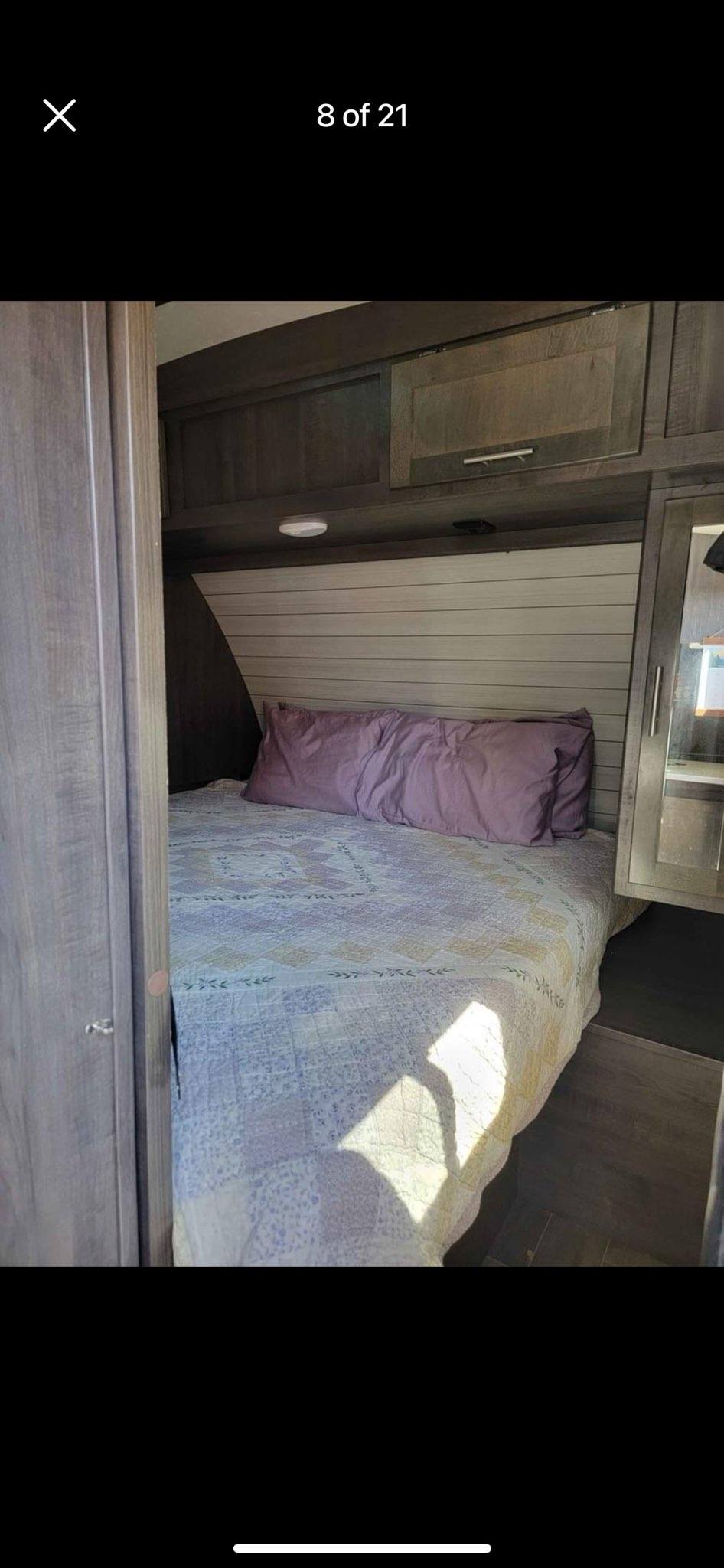 Cozy RV rental bedroom featuring a bed with purple pillows, overhead wood cabinets, and built-in storage.. Crossroads RV Sunset Trail Super Lite 2019