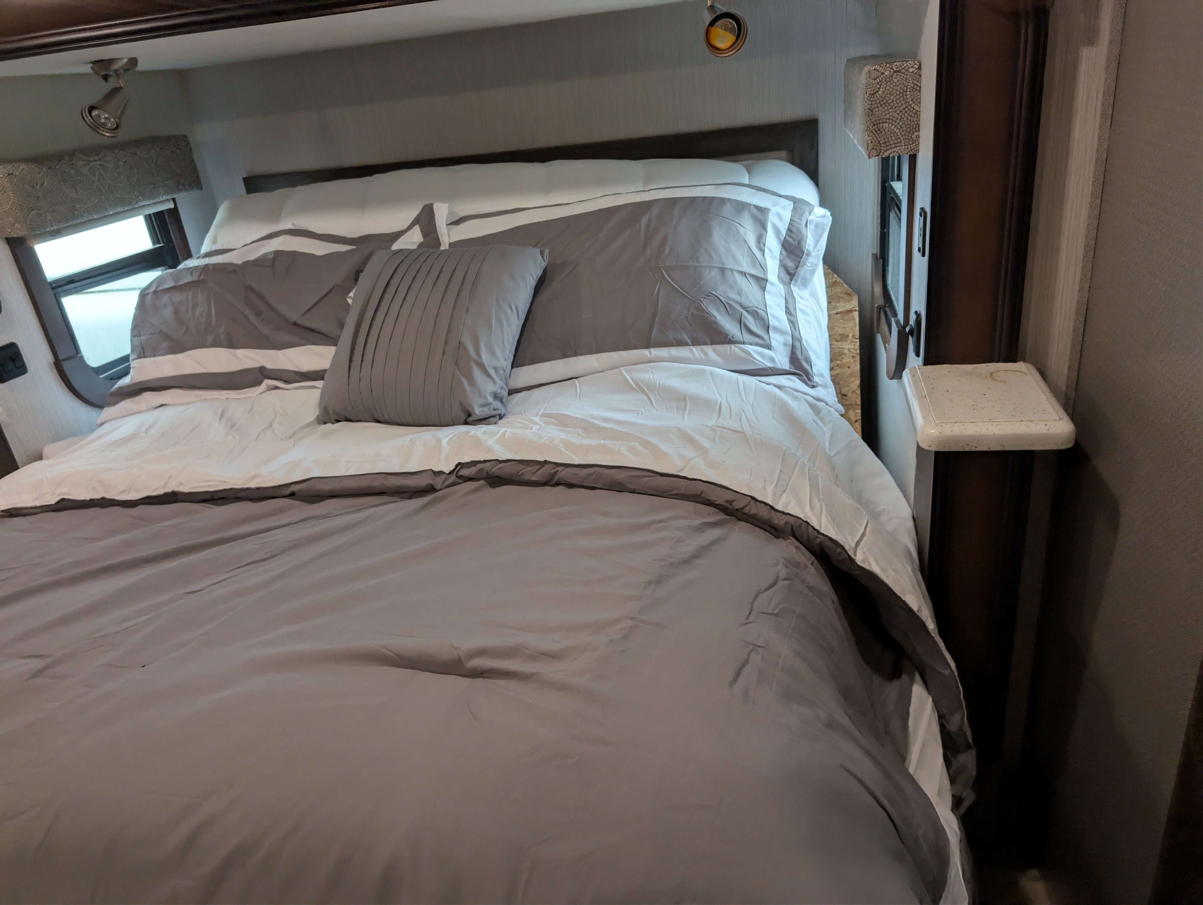 RV rental bedroom: modern grey & white bedding on a comfortable bed, overhead lighting, & window view.. Heartland RVs Landmark 365 2020