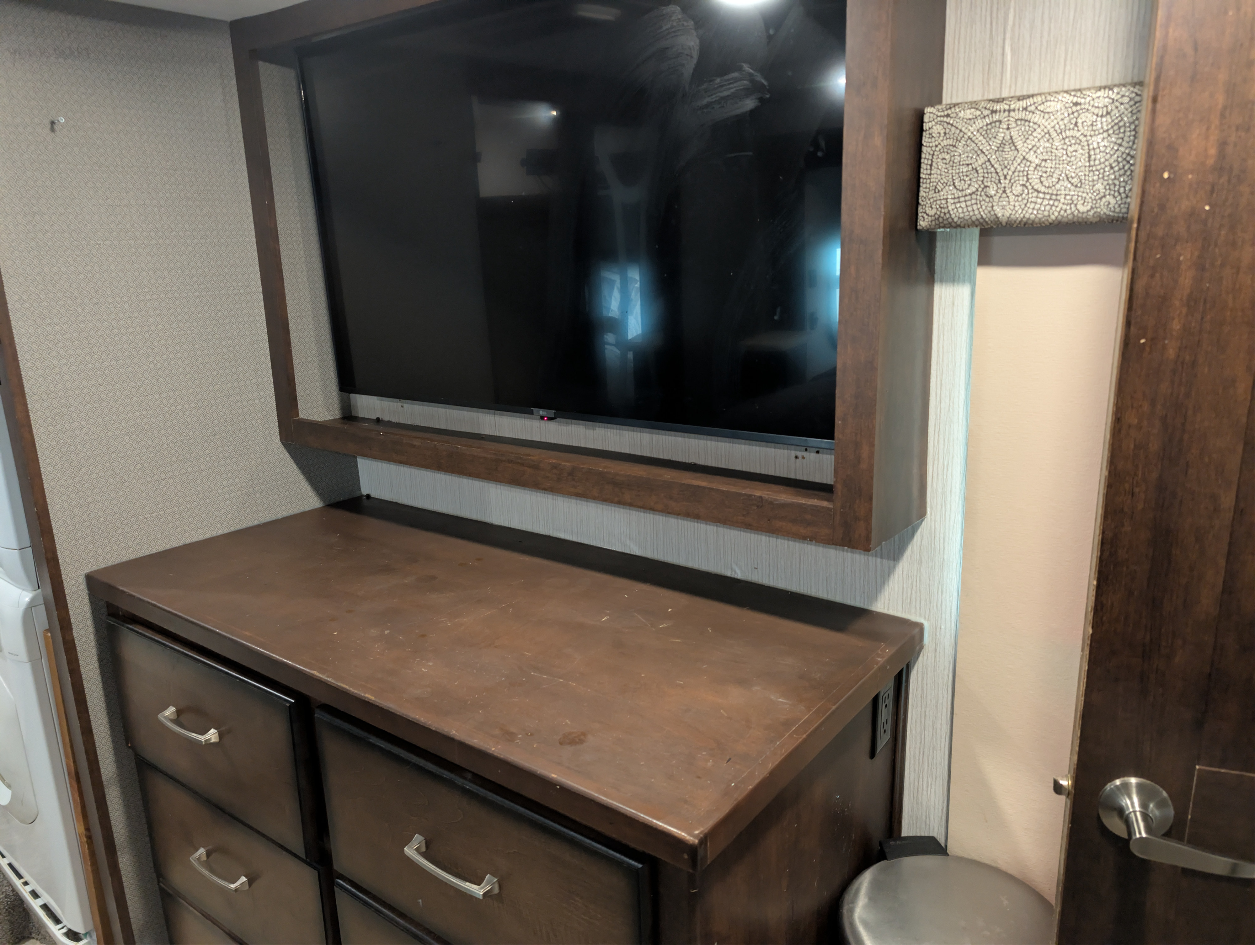 RV rental interior: Wall-mounted TV over a dark wood dresser with drawers, laundry unit left, door right. Ample storage.. Heartland RVs Landmark 365 2020