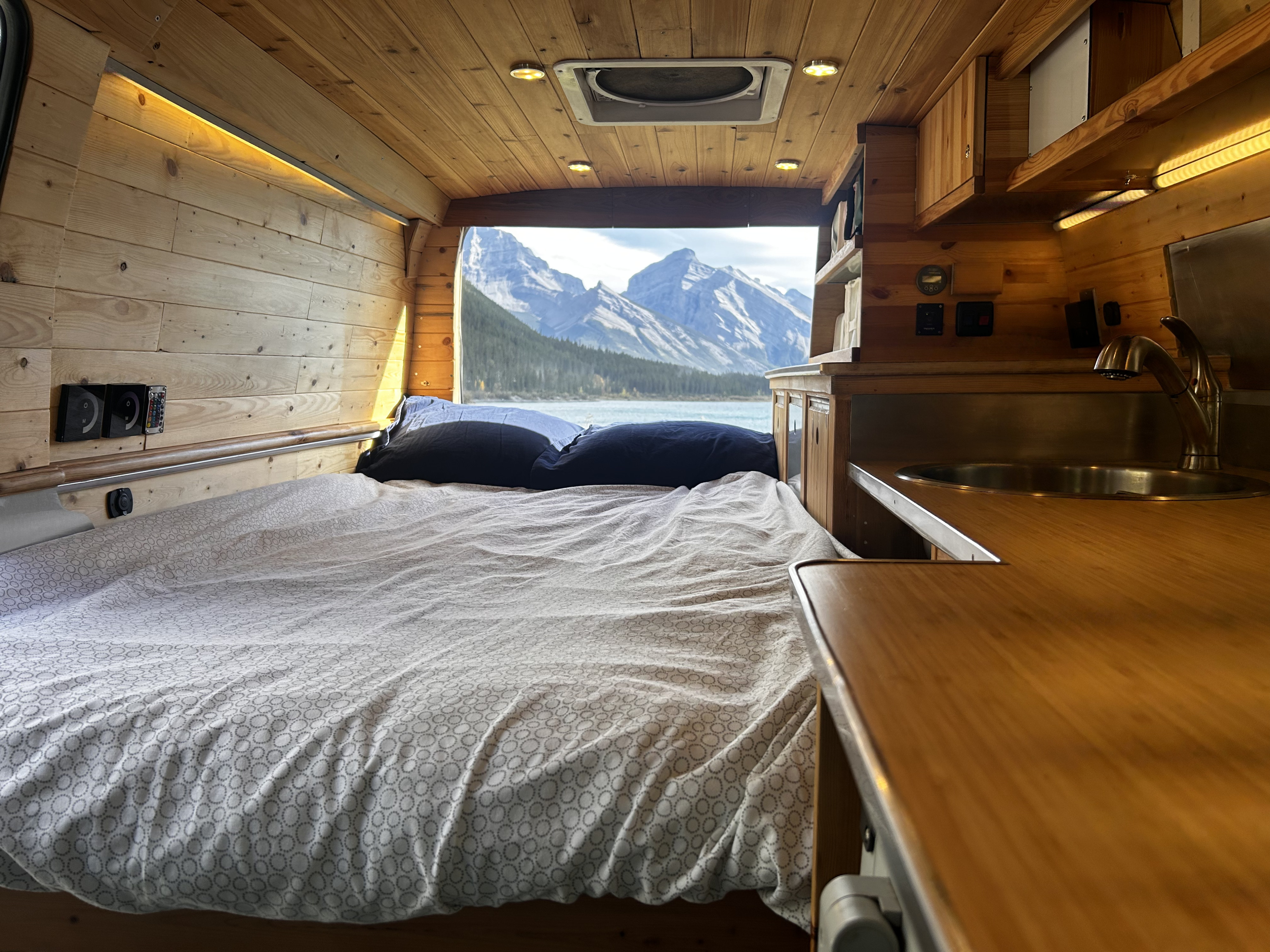Enjoy the ultimate rv rental experience! A cozy camper van interior with a bed, kitchenette, and stunning mountain lake view.. Ford Econoline 2009