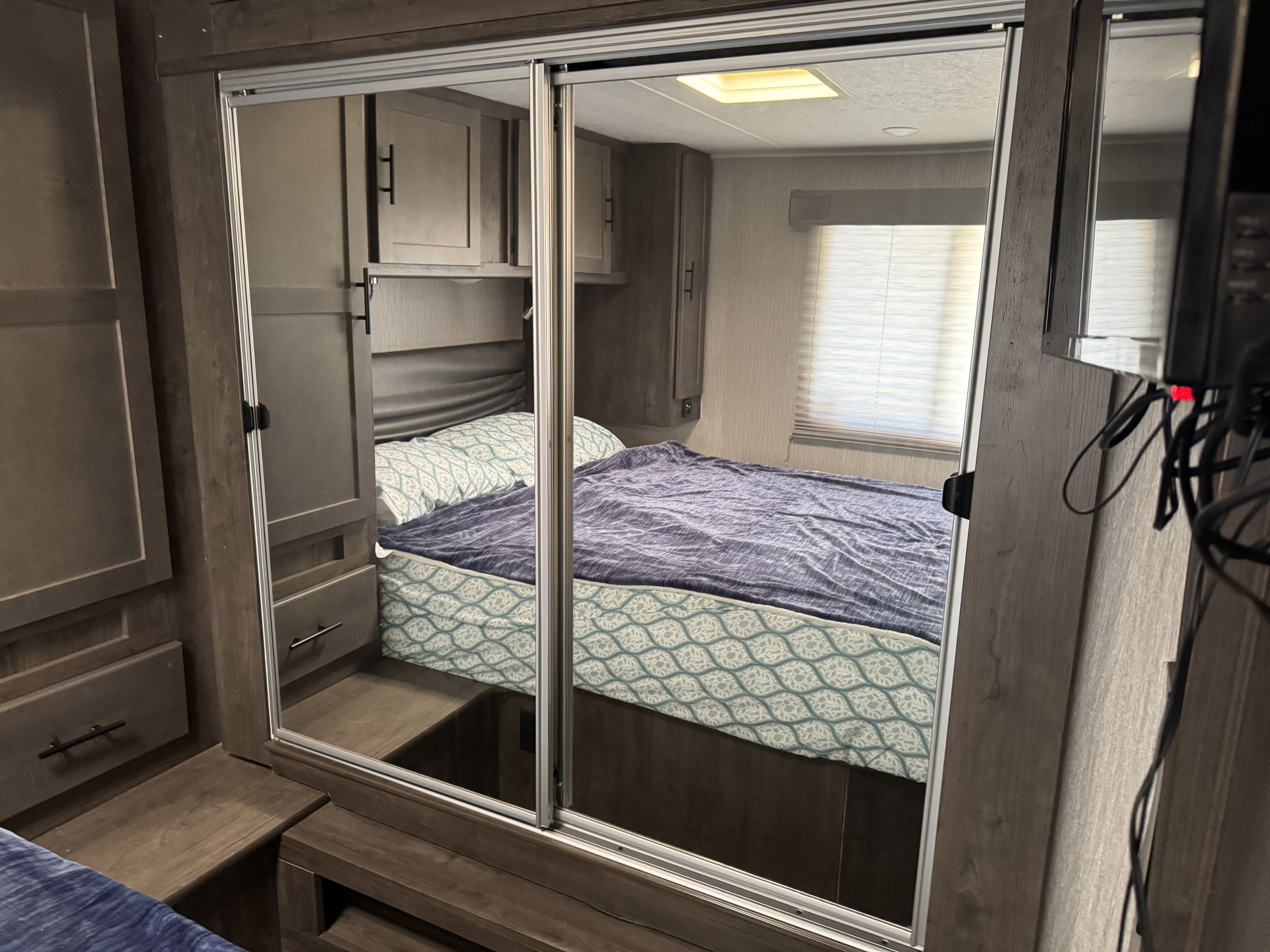 RV rental bedroom with sliding mirrored closets reflecting a comfy bed, window, and cabinetry for optimized space.. Coach House coachmen leprechaun 2022