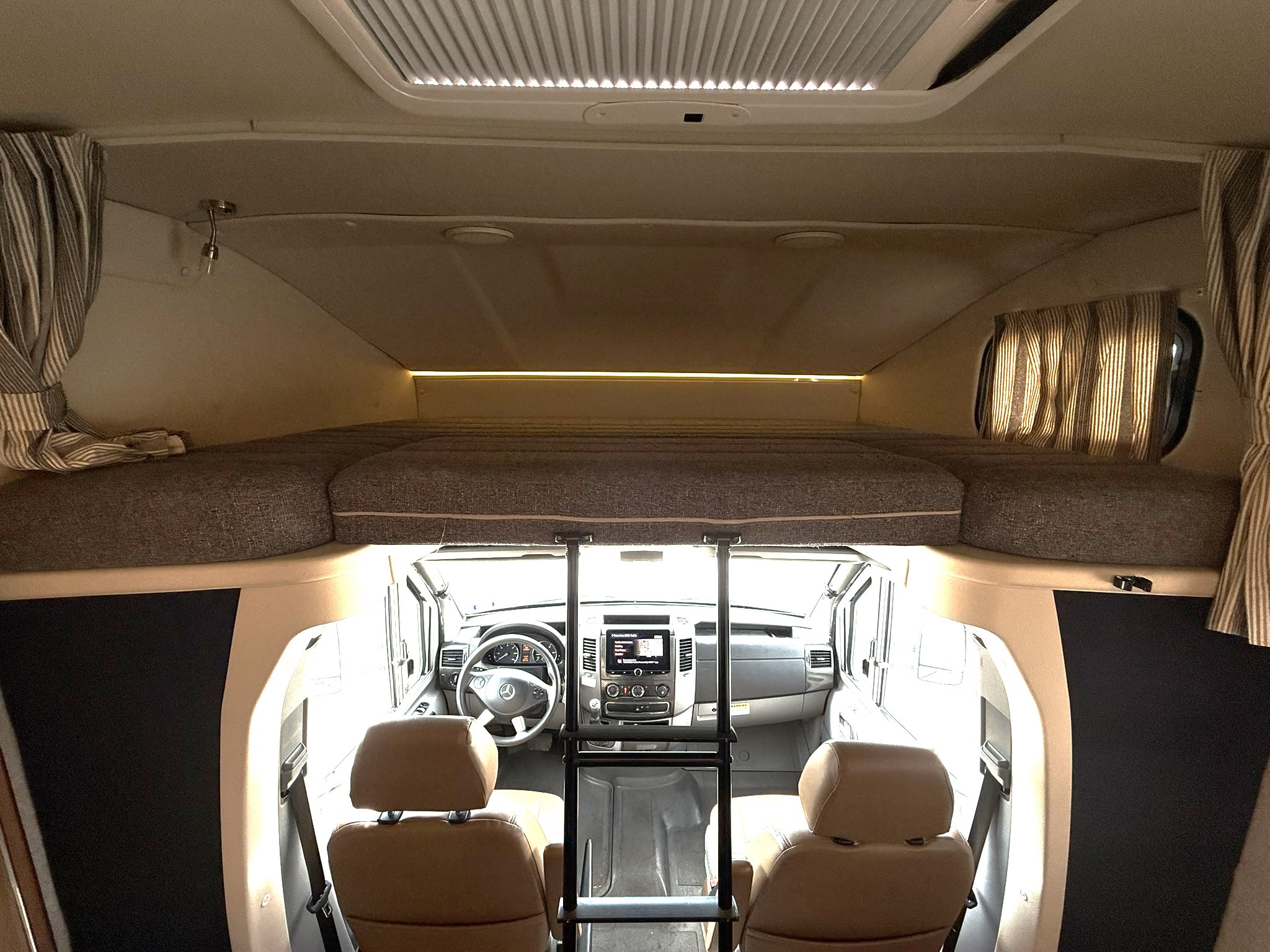 Cozy over-cab bunk bed & ladder in an RV rental, overlooking the front cockpit and dashboard.. Winnebago View 2019