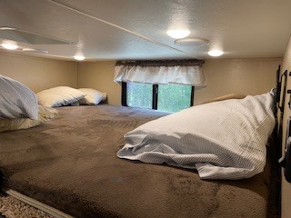Cozy RV rental over-cab sleeping area: a large bed with brown comforter, pillows, and window for comfortable travel.. Forest River Coachmen Chaparral 2017