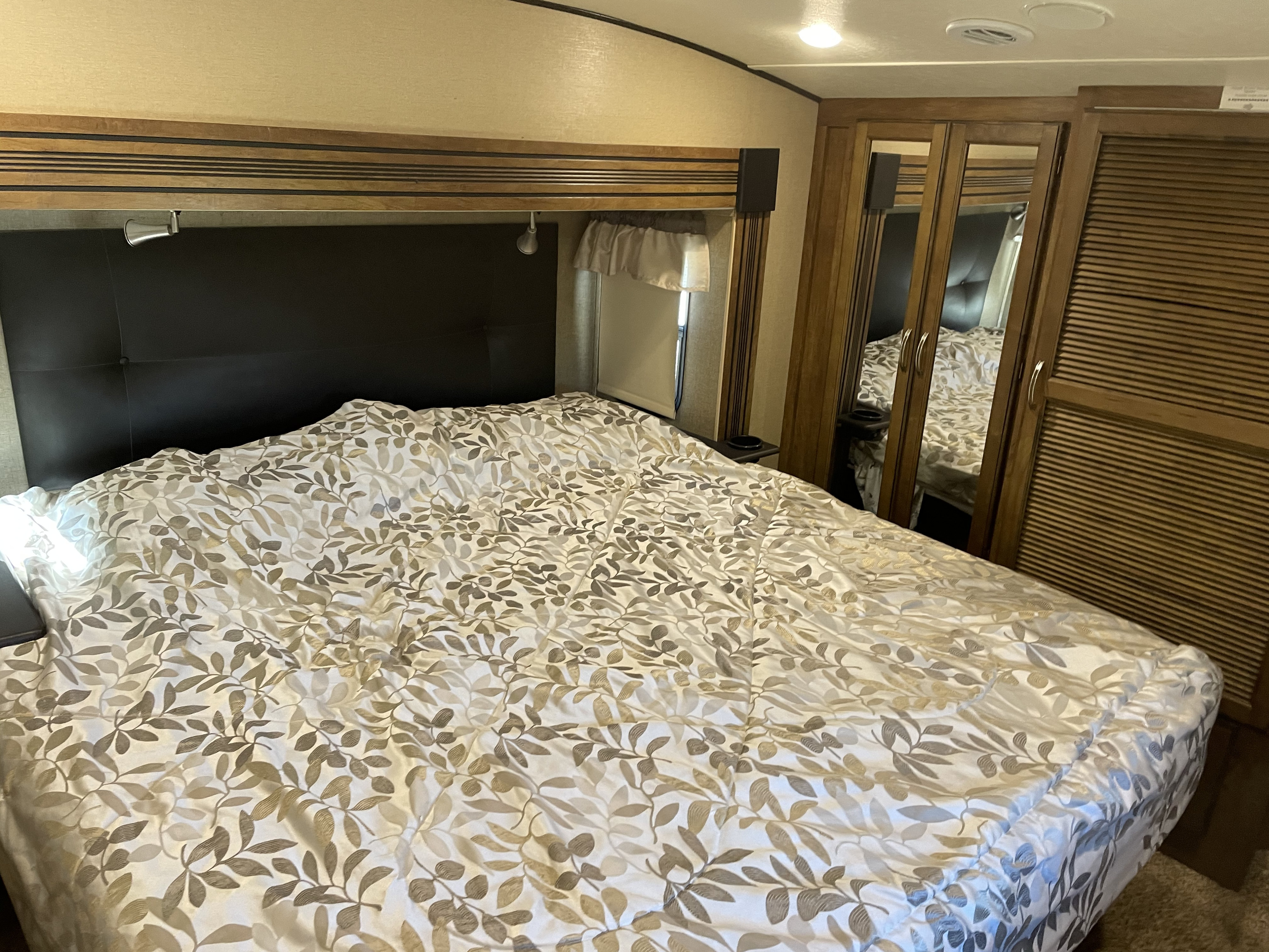 Comfortable RV rental bedroom featuring a bed with a leaf-patterned comforter, dark headboard, and wood-paneled storage.. Forest River Coachmen Chaparral 2017
