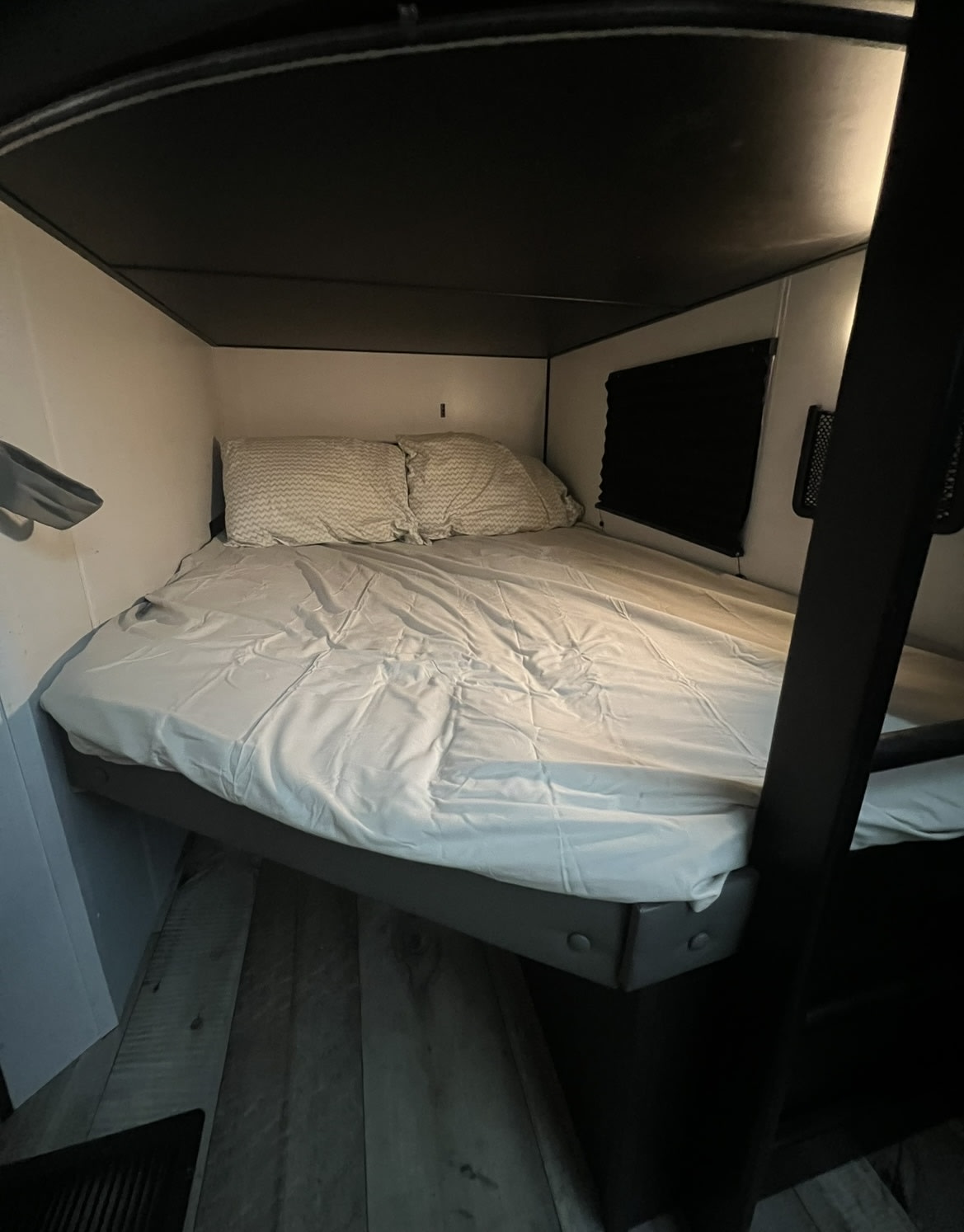A comfortable sleeping area in an RV rental, featuring a bed with white sheets, patterned pillows, dark ceiling, and a window blind.. Keystone RV Springdale 2022