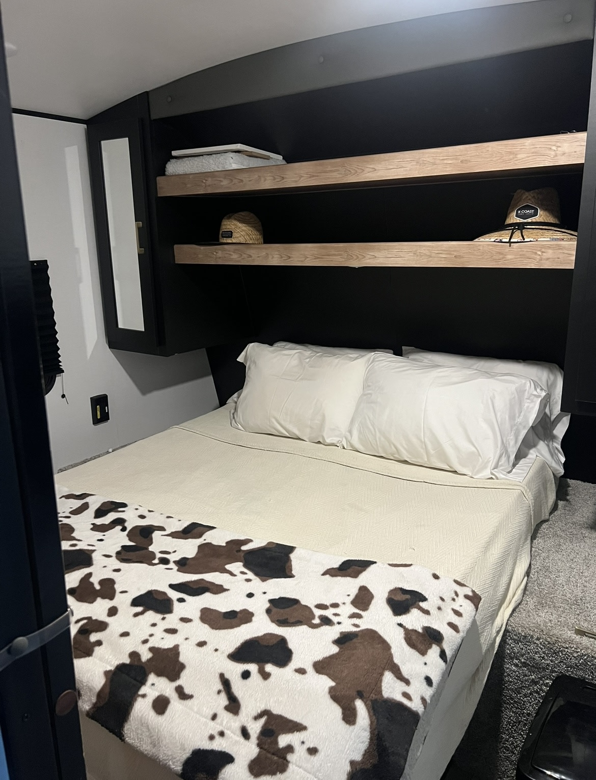 Cozy RV rental bedroom with a white bed, cow print blanket, and sleek overhead storage with hats.. Keystone RV Springdale 2022