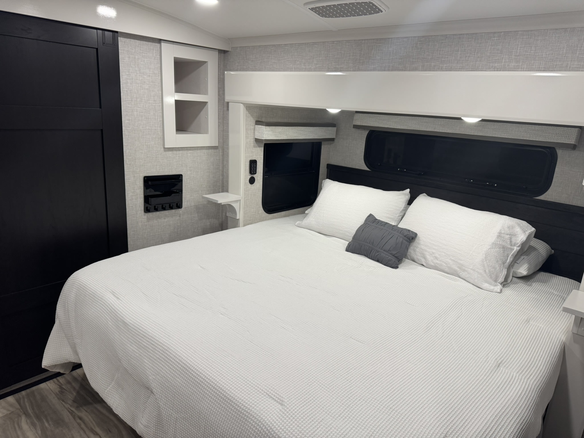 Inside a stylish RV rental bedroom, featuring a large bed with white bedding, dark wood accents, and clever storage.. Jayco Pinnacle 2025