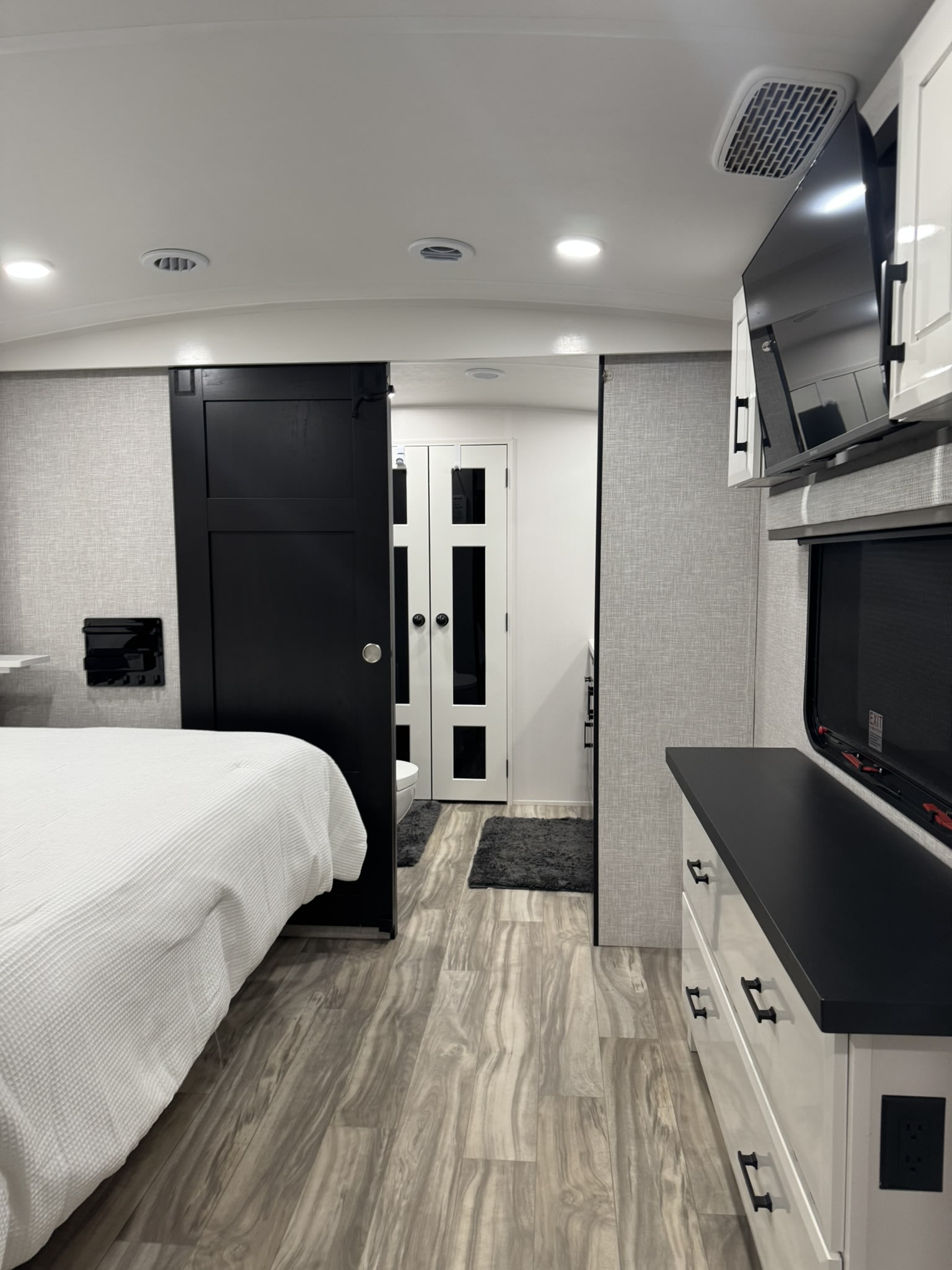 This modern RV rental interior showcases a bedroom with a white bed, a black sliding barn door leading to a bathroom, and a dresser with TV.. Jayco Pinnacle 2025