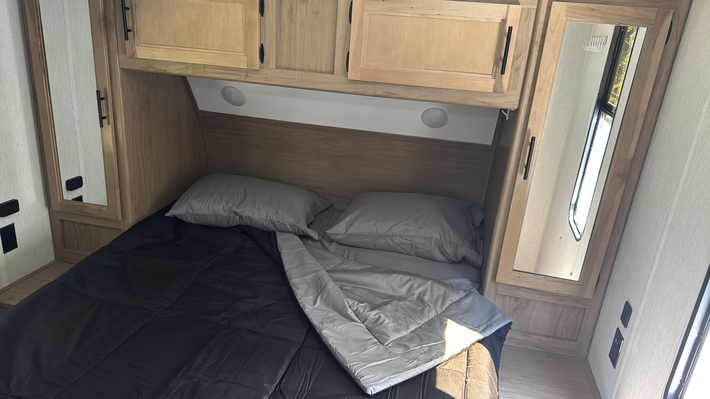 An RV rental bedroom featuring a compact bed, overhead wooden cabinets, and mirrored wardrobes for a functional space.. Forest River Cherokee Grey Wolf 2023