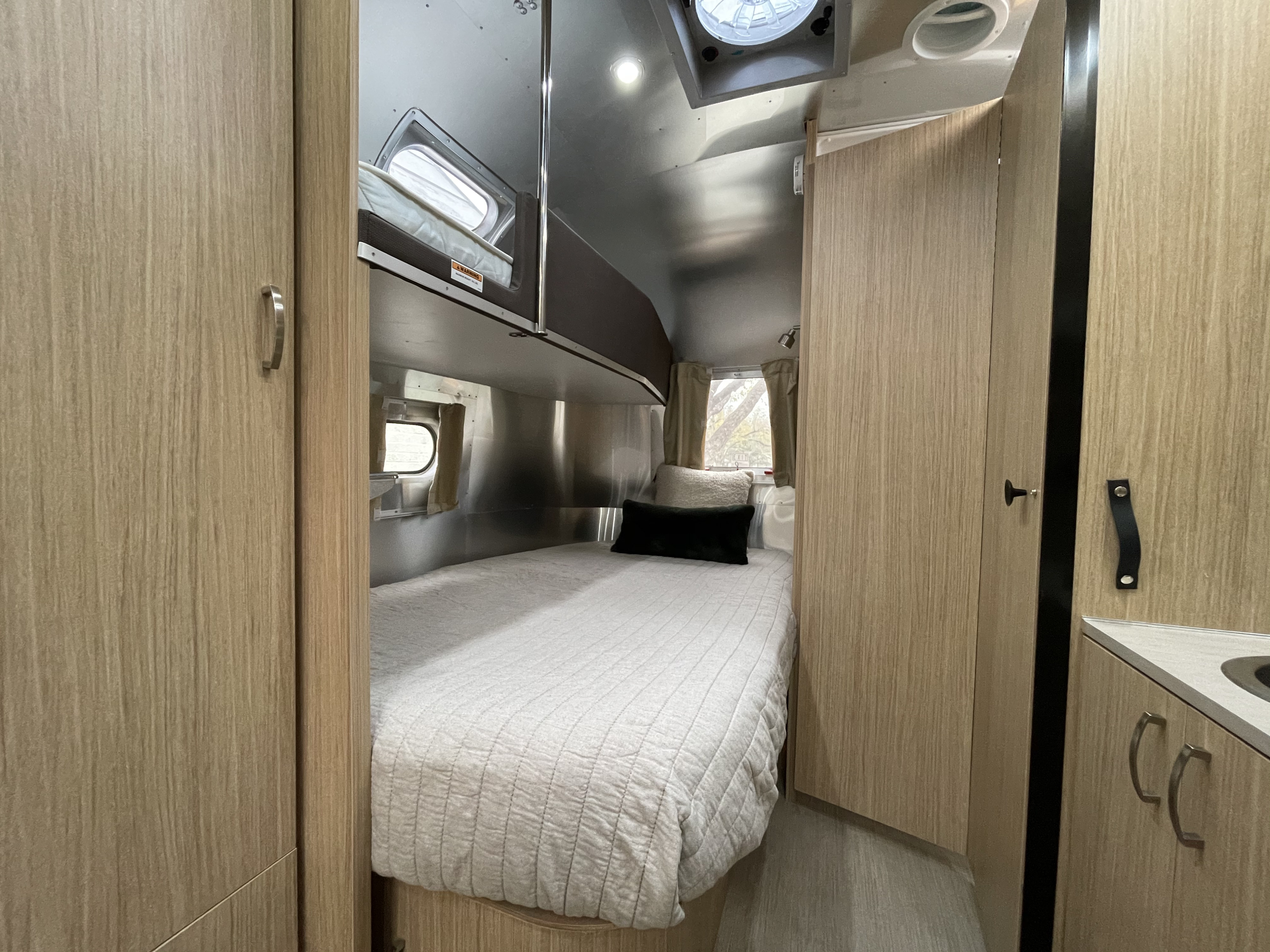 RV rental: A cozy bedroom space with a bed, upper bunk, light wood cabinets, and polished metal walls in a travel trailer.. Airstream Flying Cloud 2018
