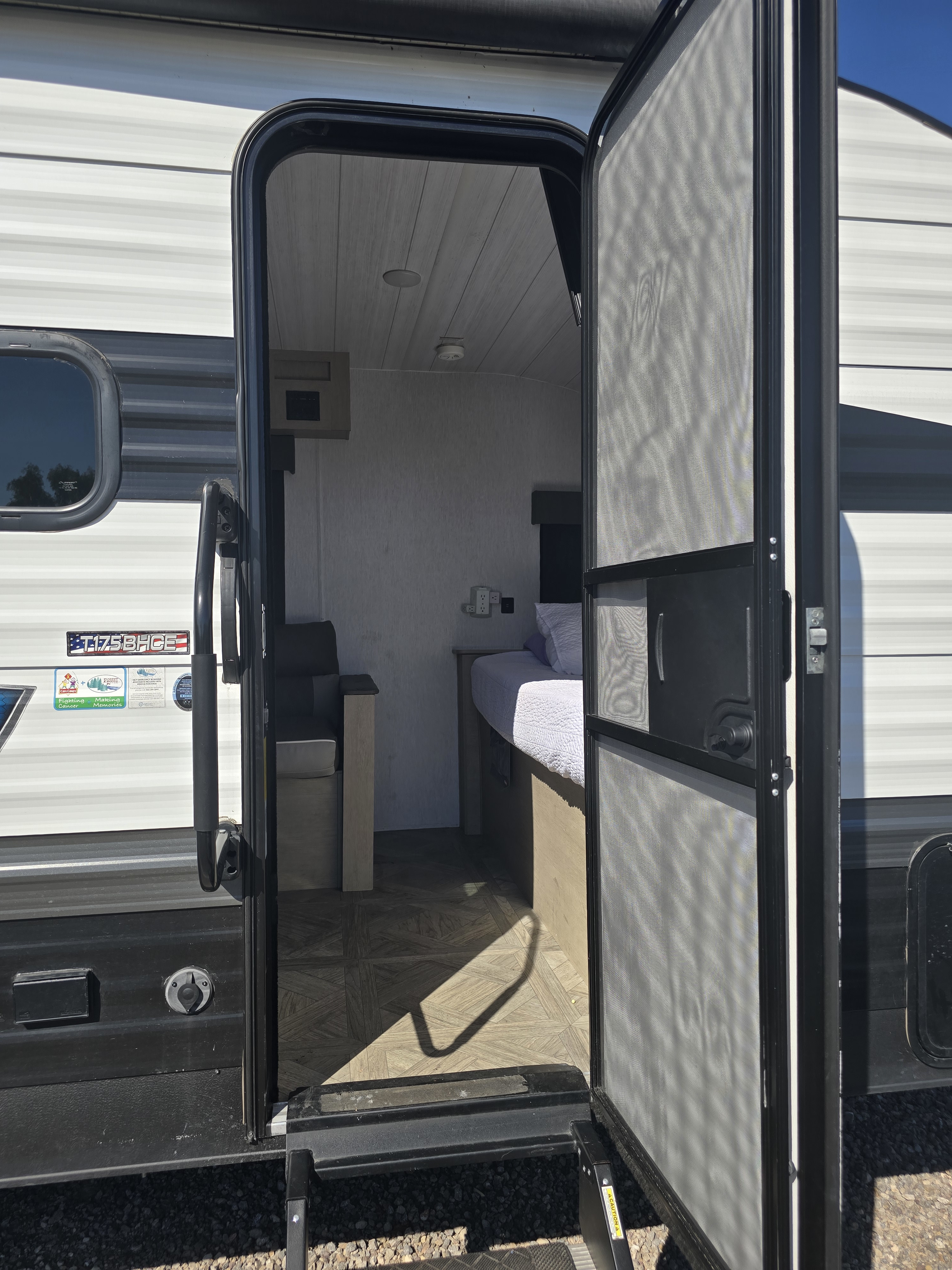 Open RV rental door showing a cozy interior with bed, dinette, and screen door. Steps lead outside.. Forest River Salem Cruise Lite 2024